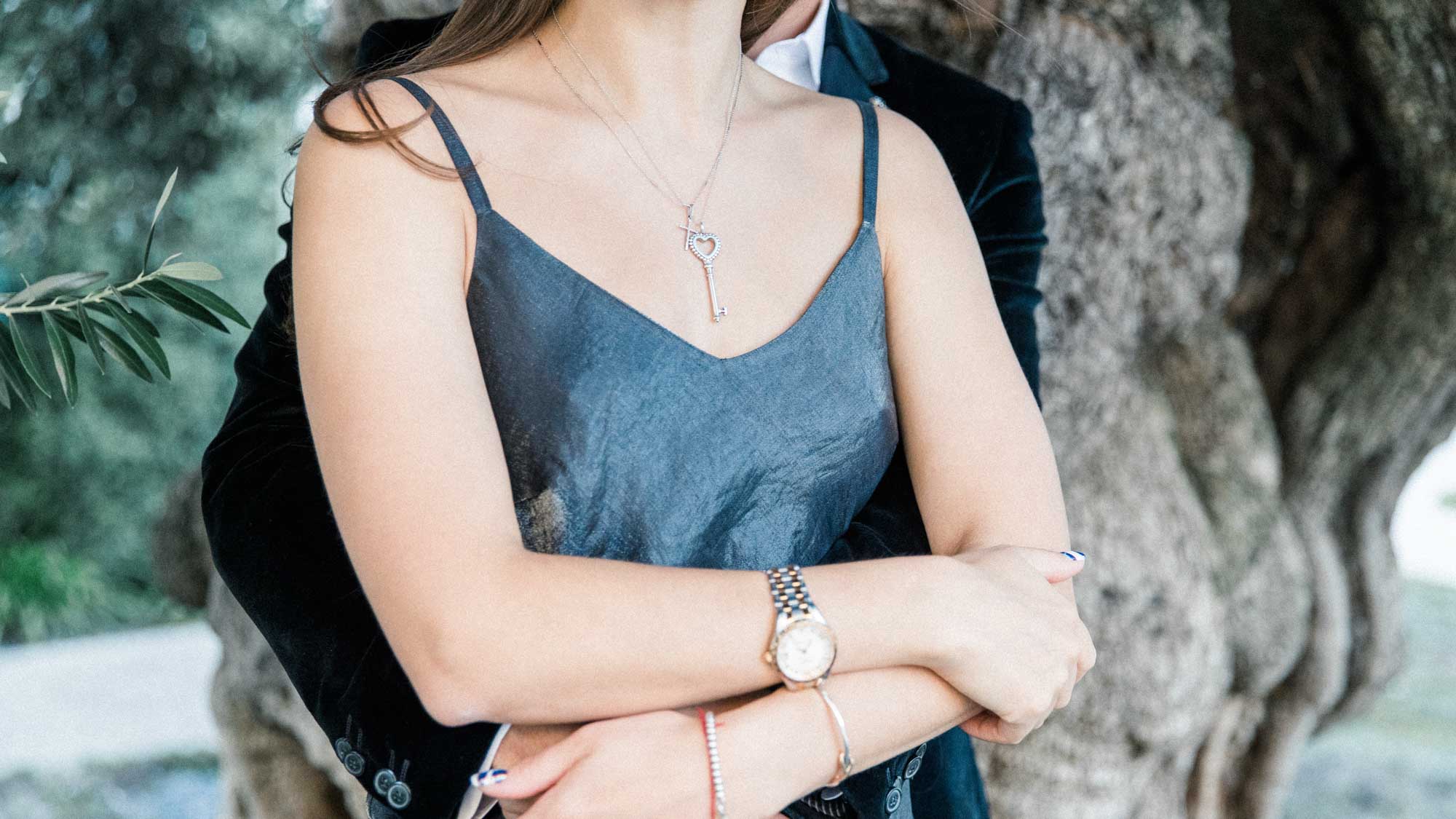 Detail of the woman's crossed arms in her partner's embrace, watch and necklace