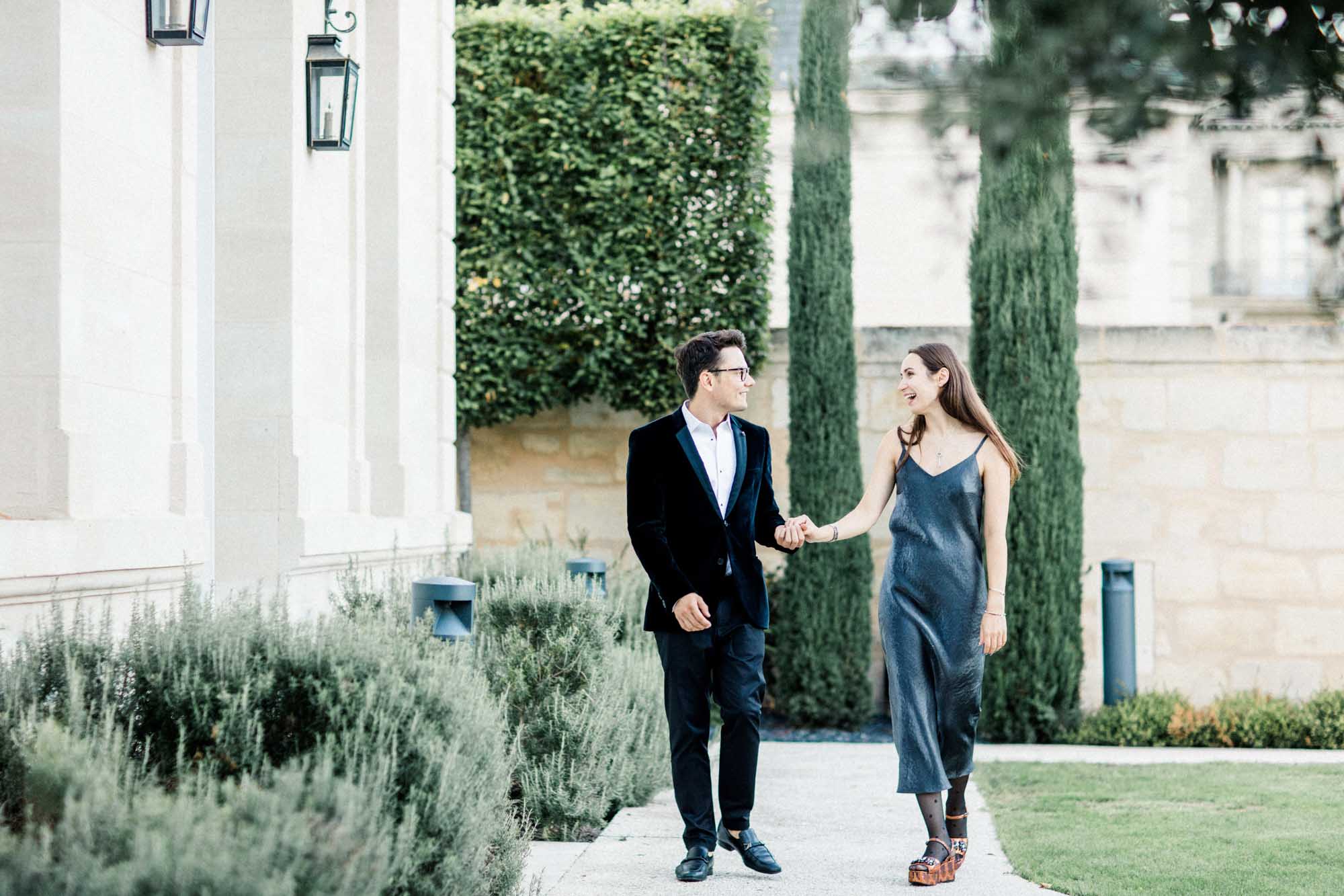 The couple walking hand in hand along the cypress-lined path