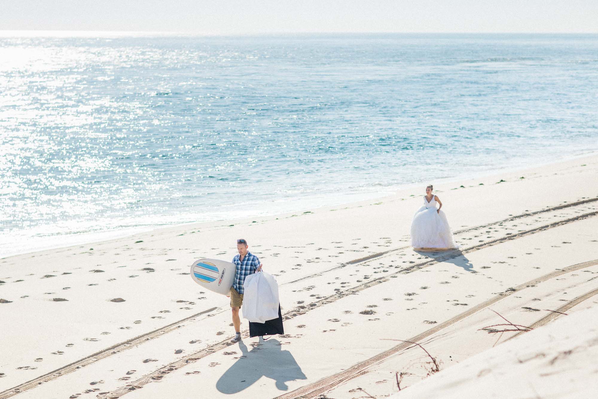 Les mariés marchent sur la plage du Cap Ferret, planche de surf sous le bras