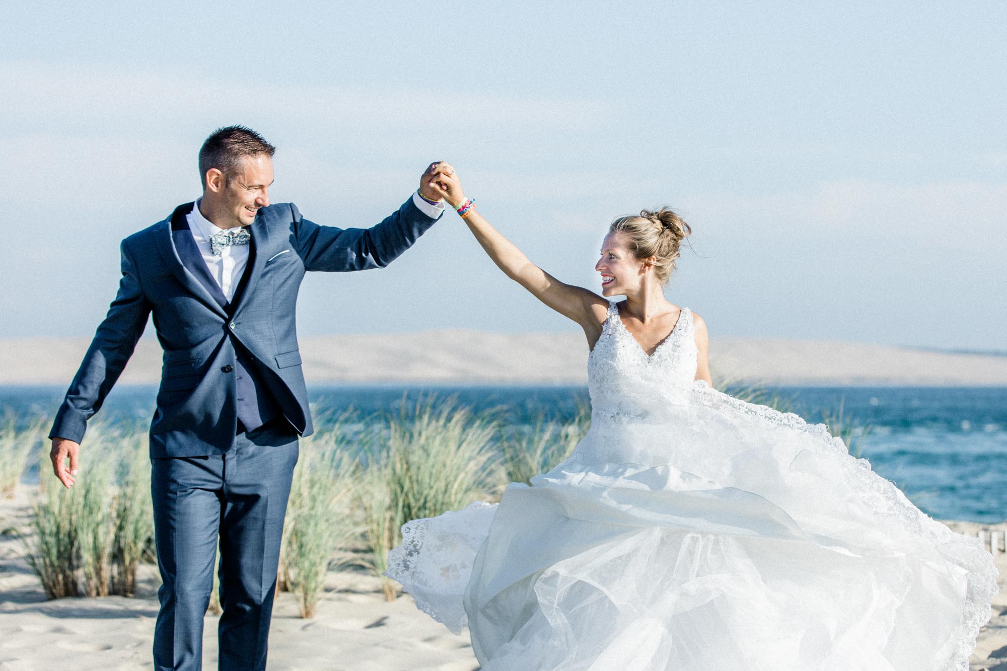 Les mariés dansent main dans la main au milieu des dunes du Cap Ferret