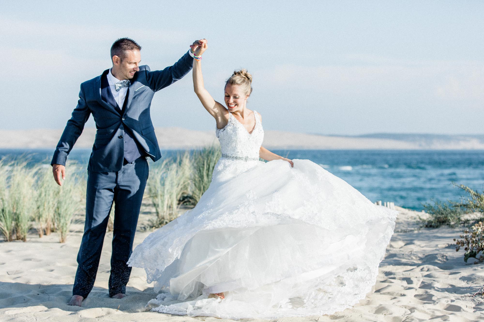 Le marié fait tourner la mariée, robe en mouvement, sur la plage