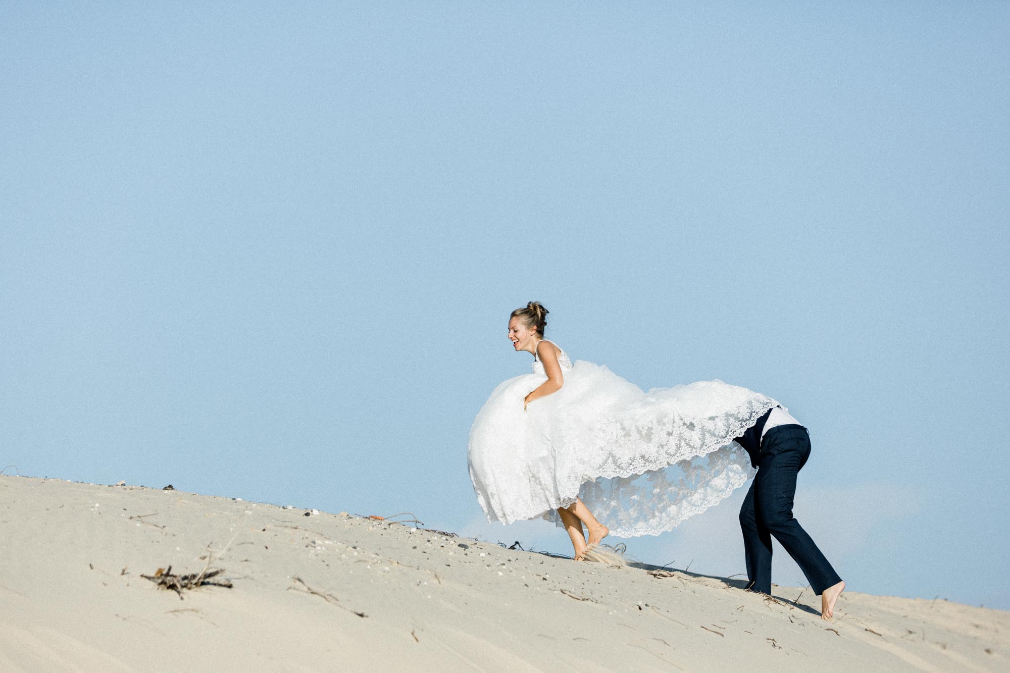 Le marié tire la mariée sur la pente d'une dune sous un ciel bleu