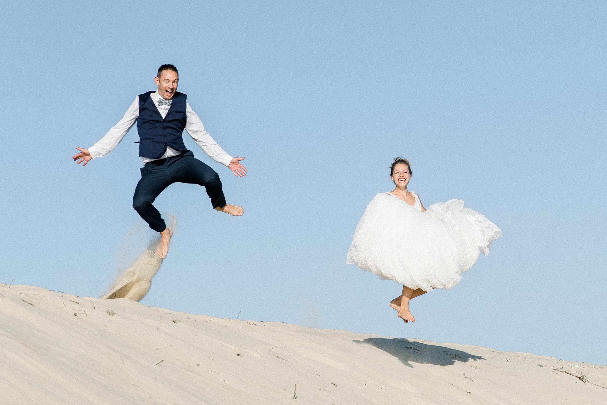Les mariés sautent dans le sable de la dune face au ciel bleu