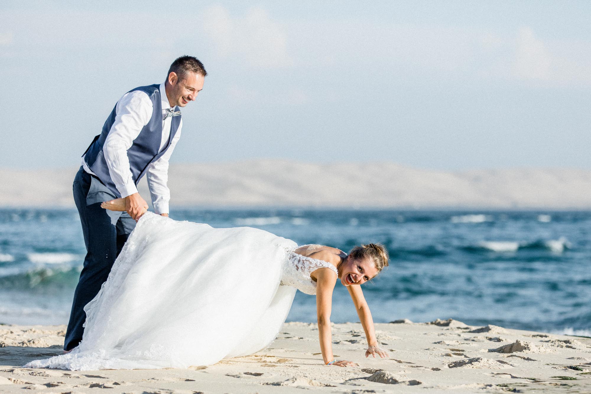 La mariée à quatre pattes dans le sable, le marié amusé à côté