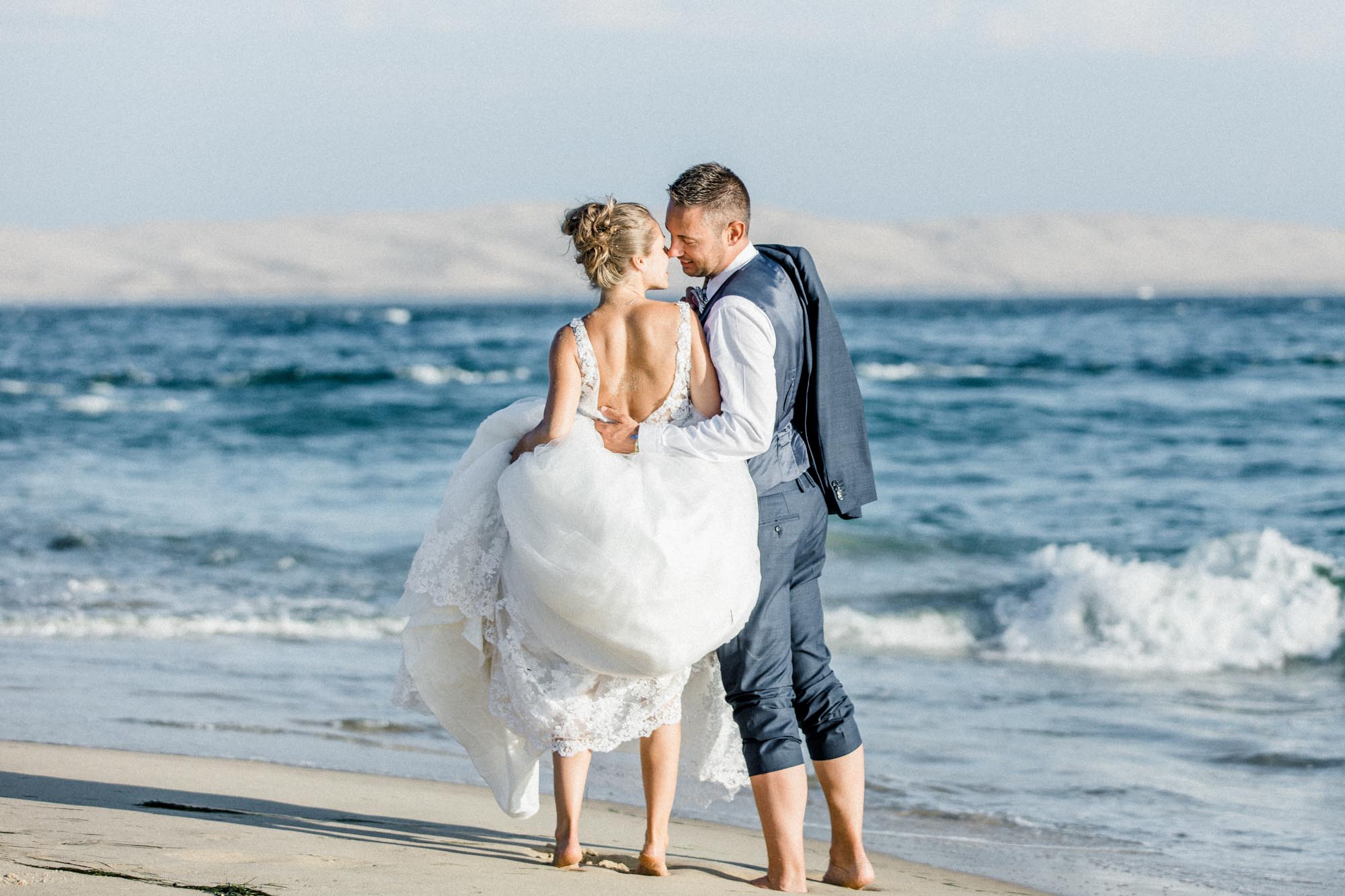 Les mariés s'embrassent au bord de l'eau, la mariée relevant sa robe