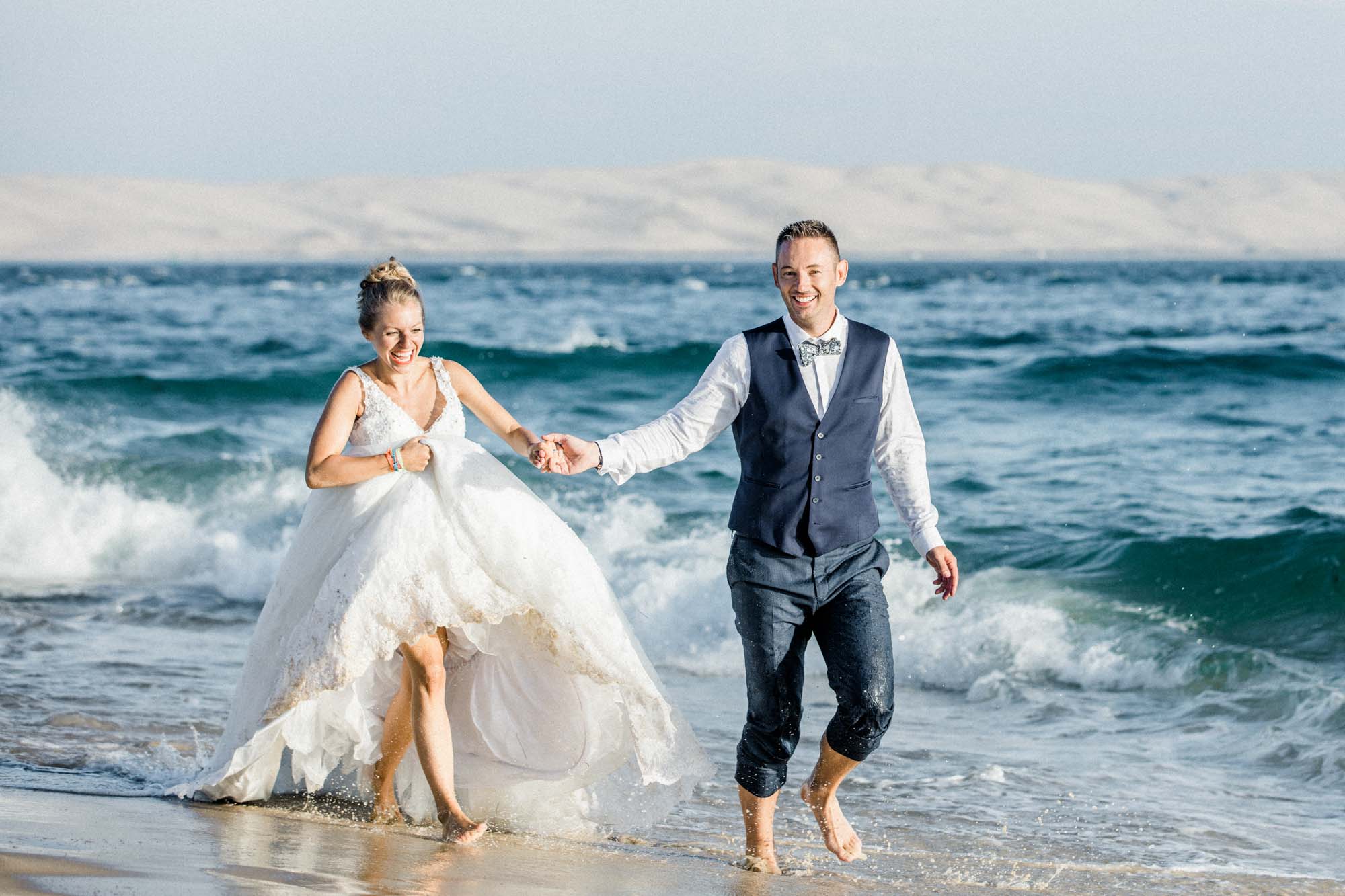 Les mariés marchent main dans la main dans les vagues du Cap Ferret