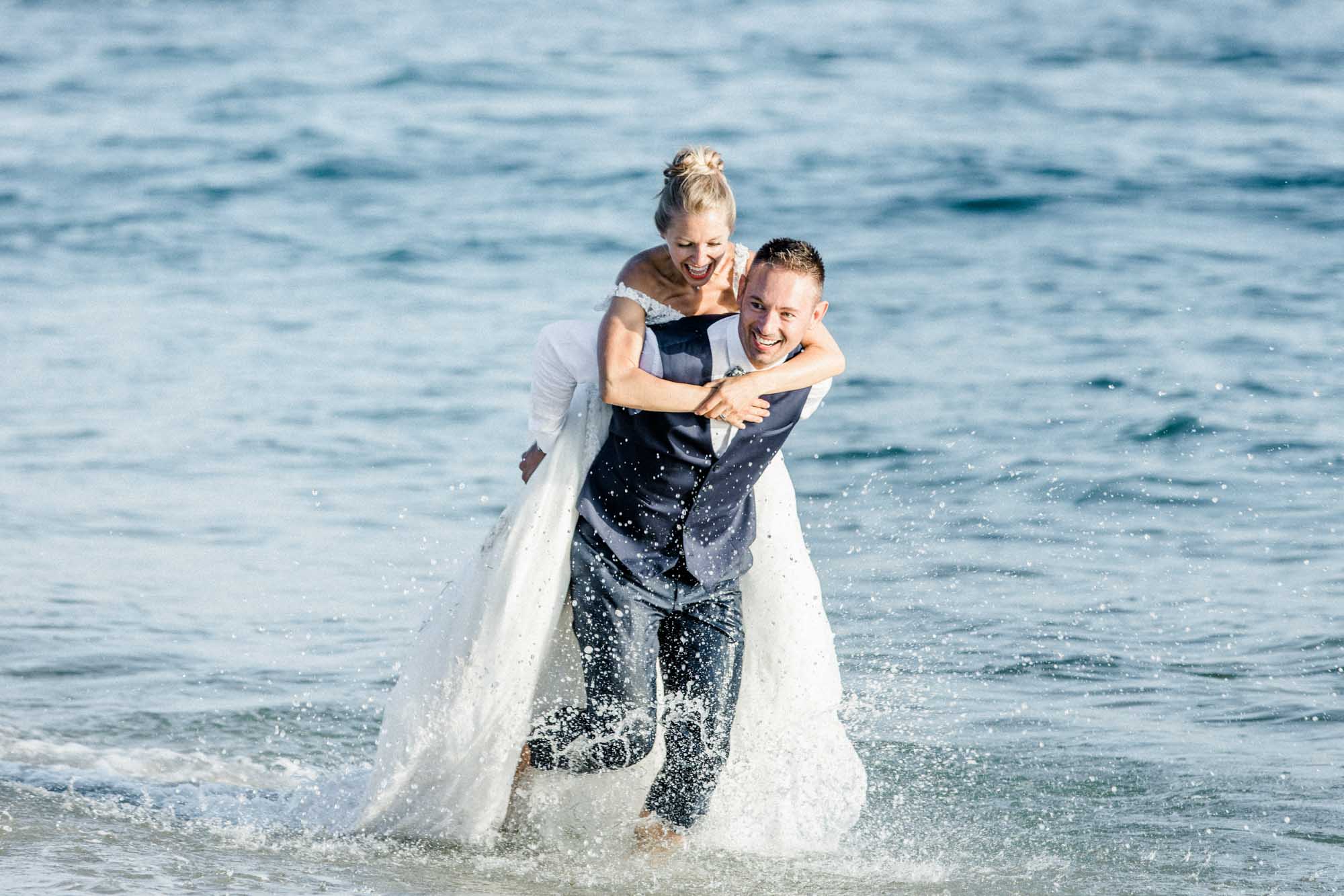 La mariée sur le dos du marié dans l'eau, éclaboussures autour d'eux