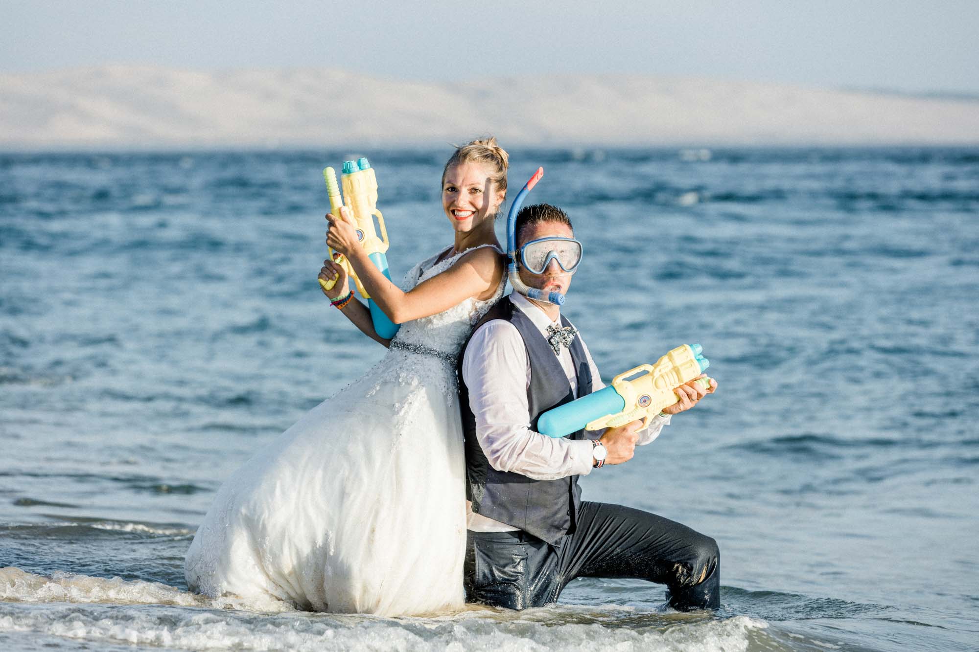Les mariés posent en riant avec leurs pistolets à eau dans les vagues