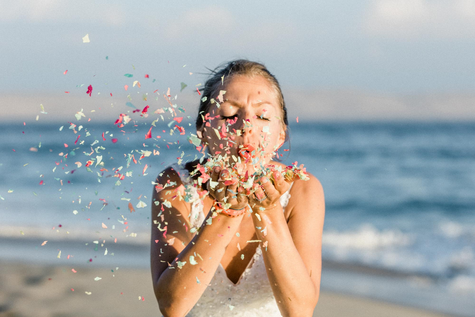 La mariée souffle des confettis colorés face à la mer