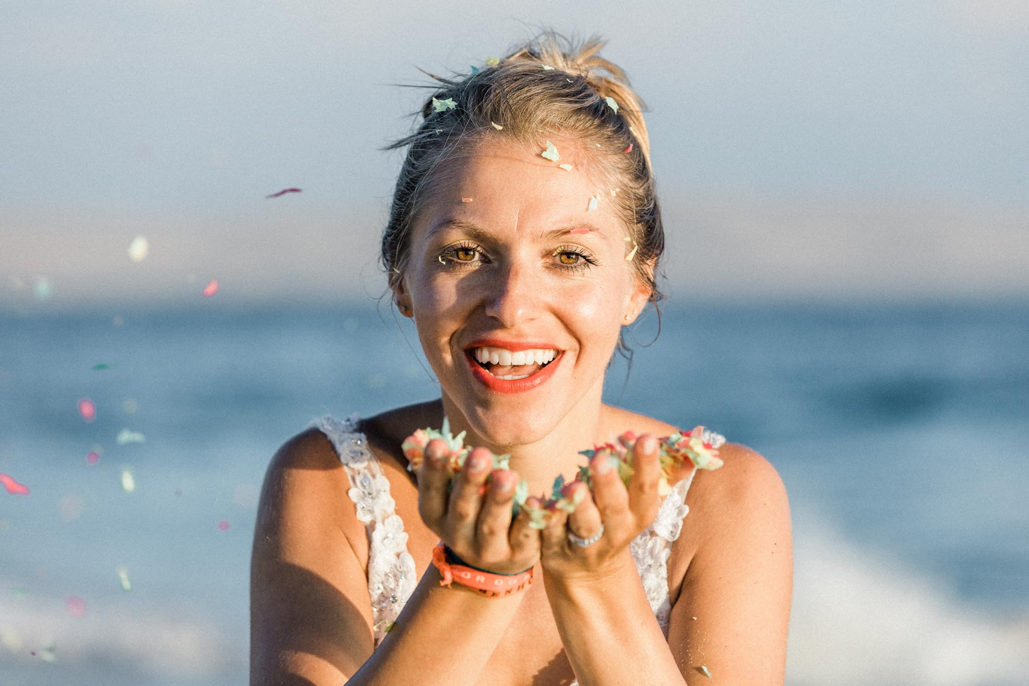 La mariée souriante tient des confettis dans ses mains en coupe