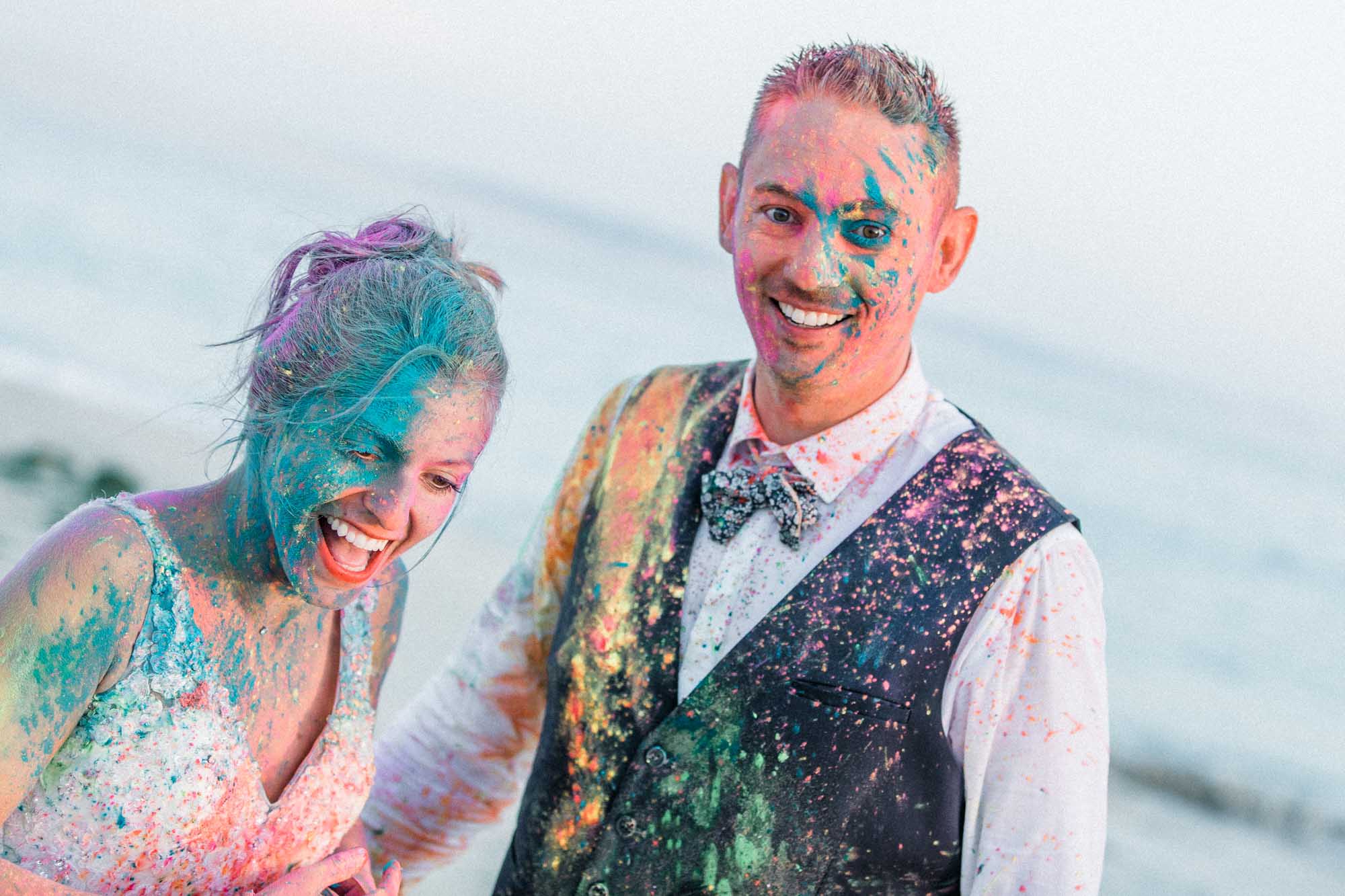 Les mariés éclatent de rire, visages couverts de poudres multicolores
