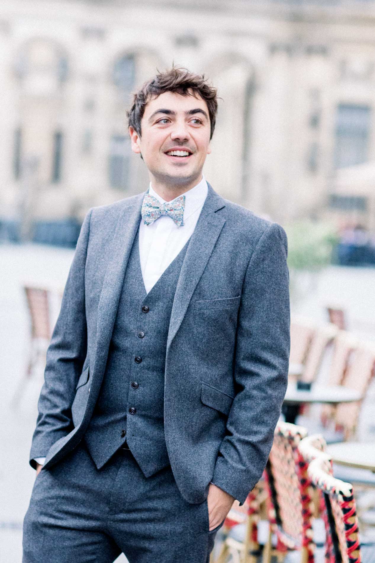 The groom in a grey three-piece suit, hands in pockets, in Bordeaux