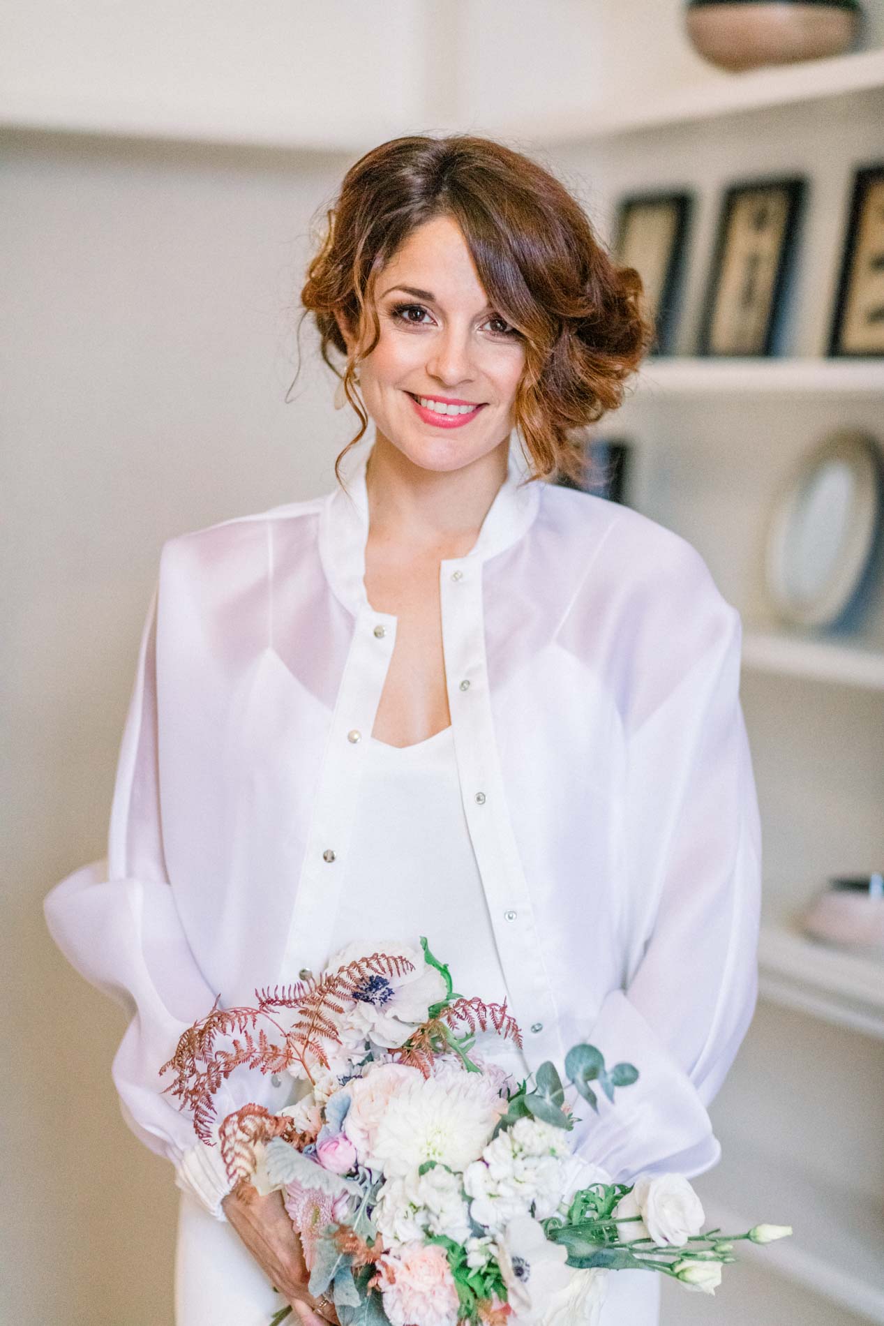 The smiling bride holding her pastel bouquet in front of a bookcase