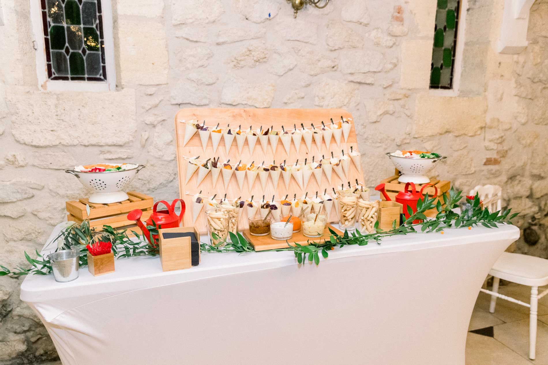 Cocktail hour buffet with paper cones and greenery against the stone wall