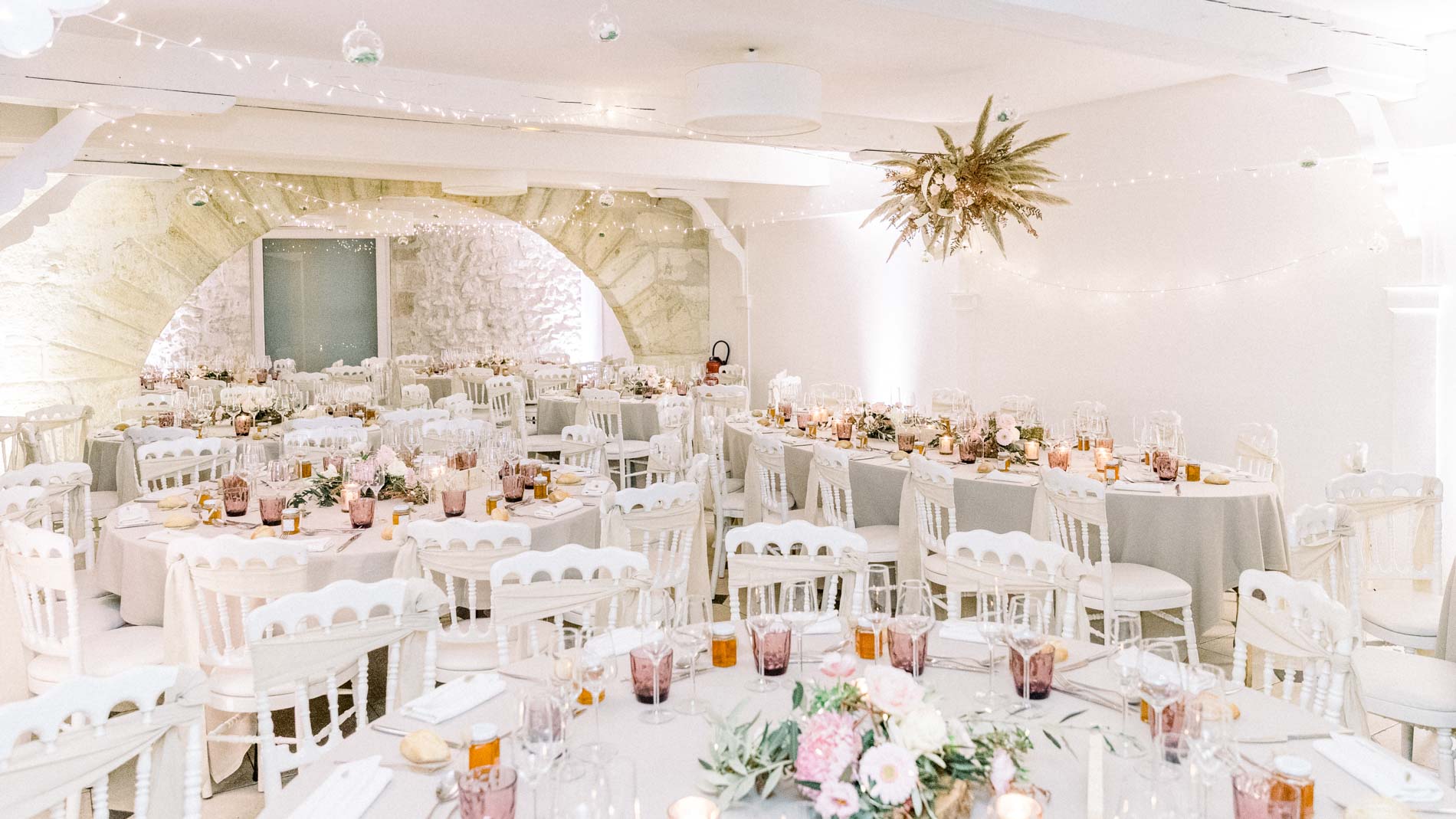 Round white-clothed tables and a hanging floral piece in the vaulted room