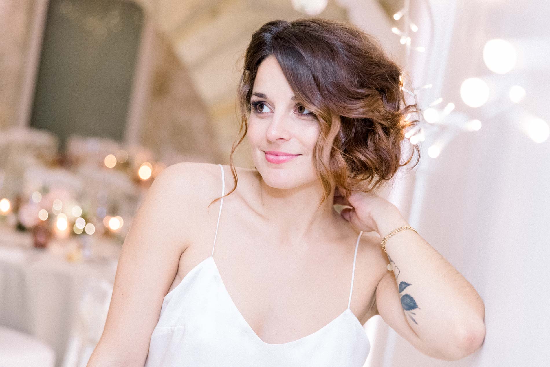 The bride smiling as she gazes across the fairy-lit reception room