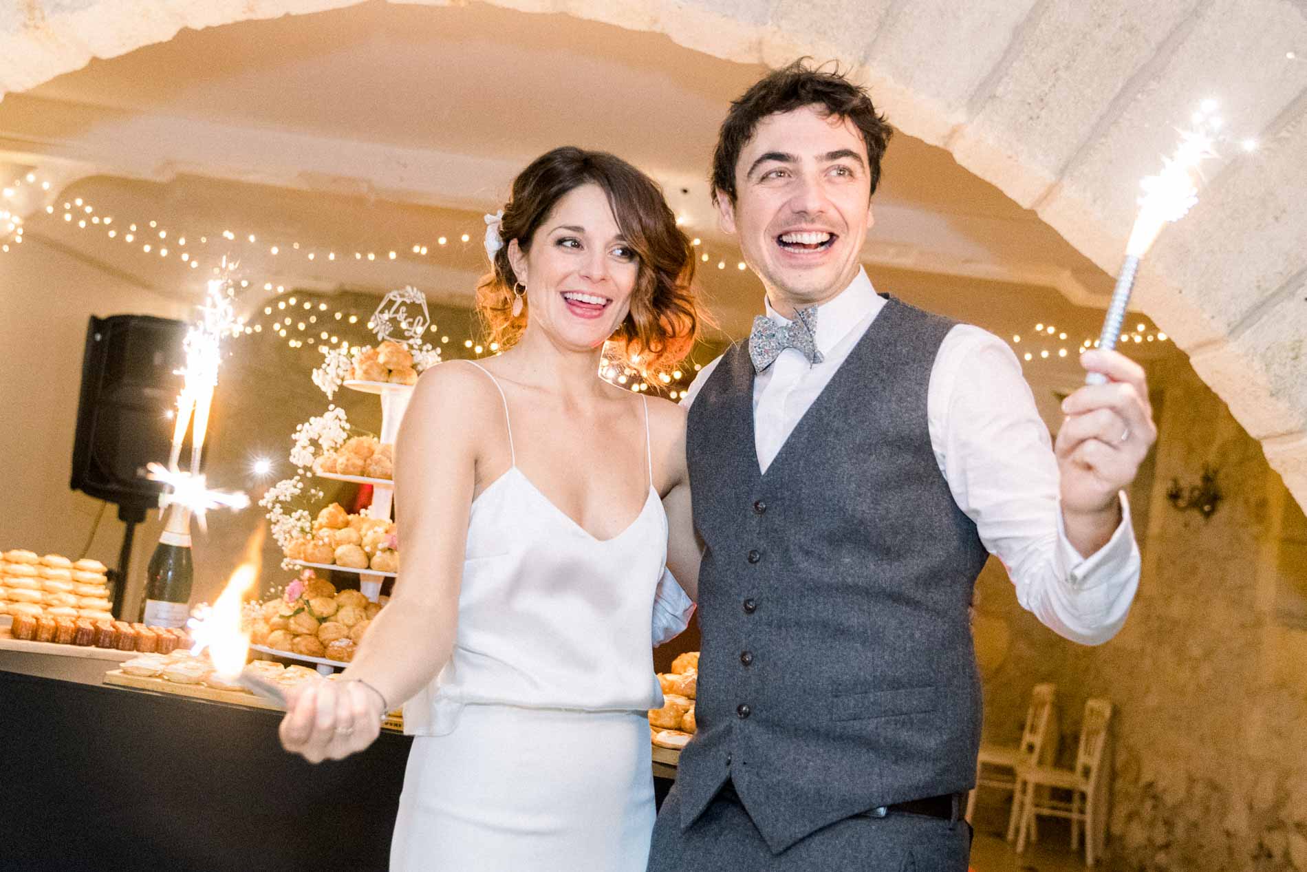 The bride and groom holding sparklers in front of the wedding dessert