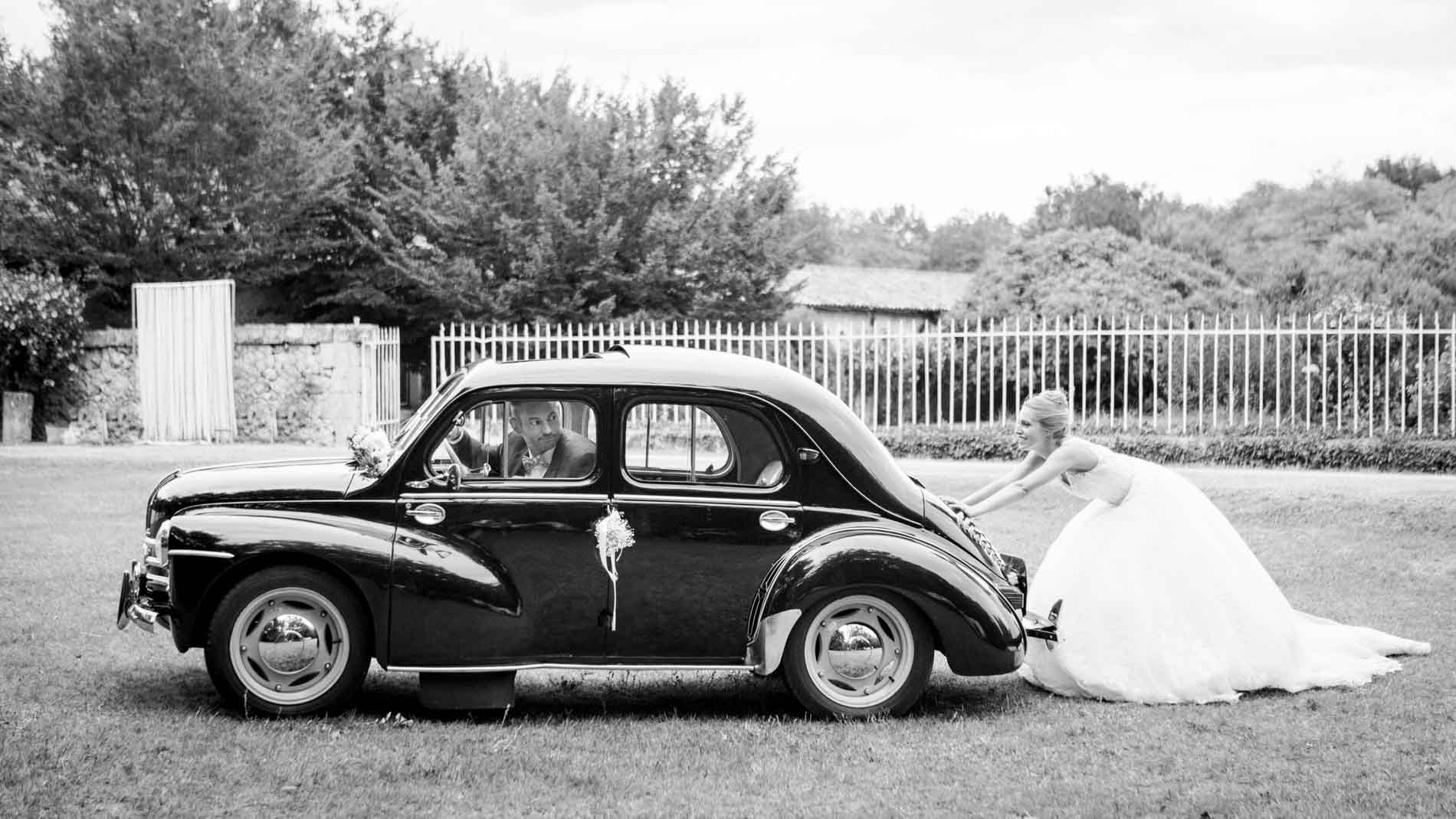 Bride sitting on the running board of a vintage car, in black and white