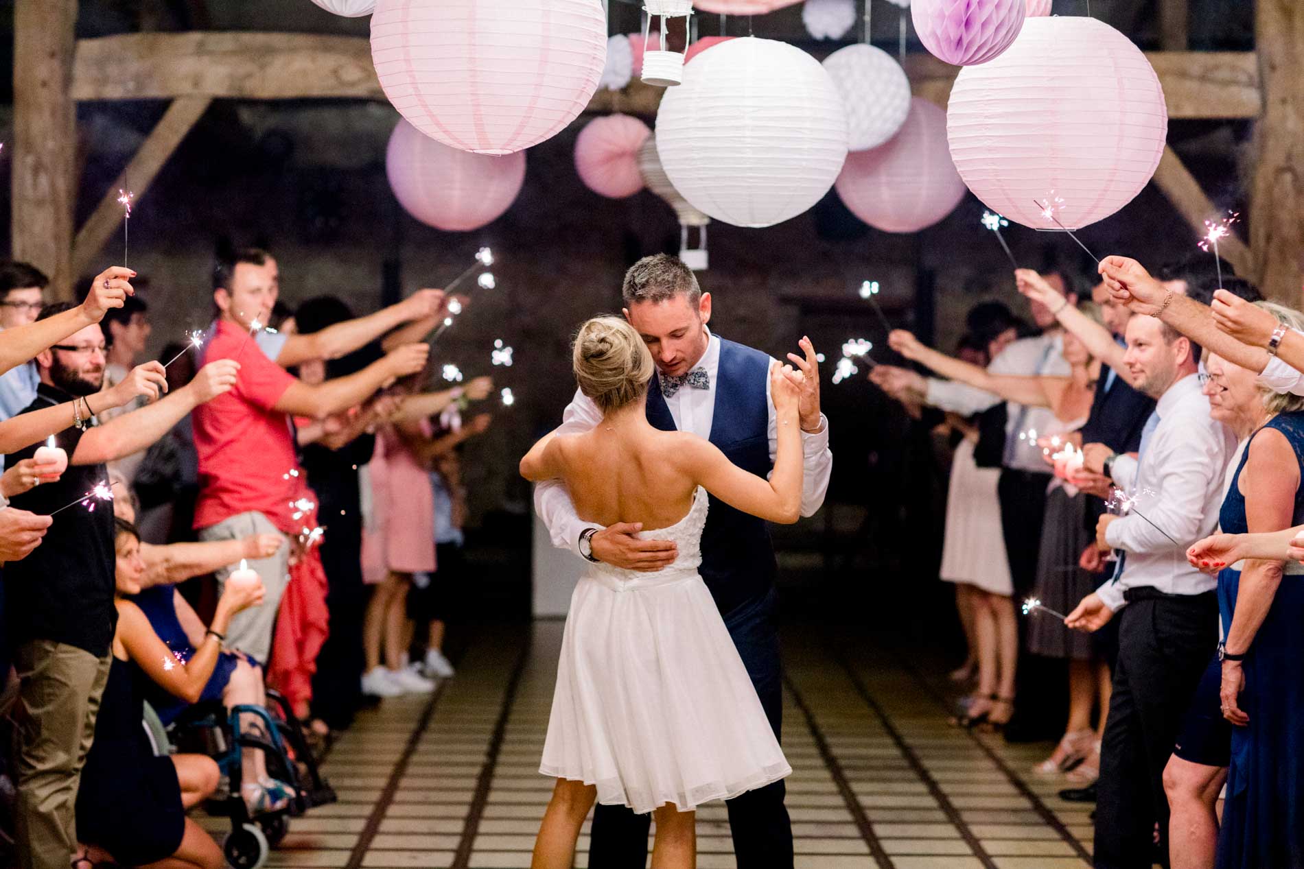 Bride and groom dancing between rows of guests beneath pink paper lanterns