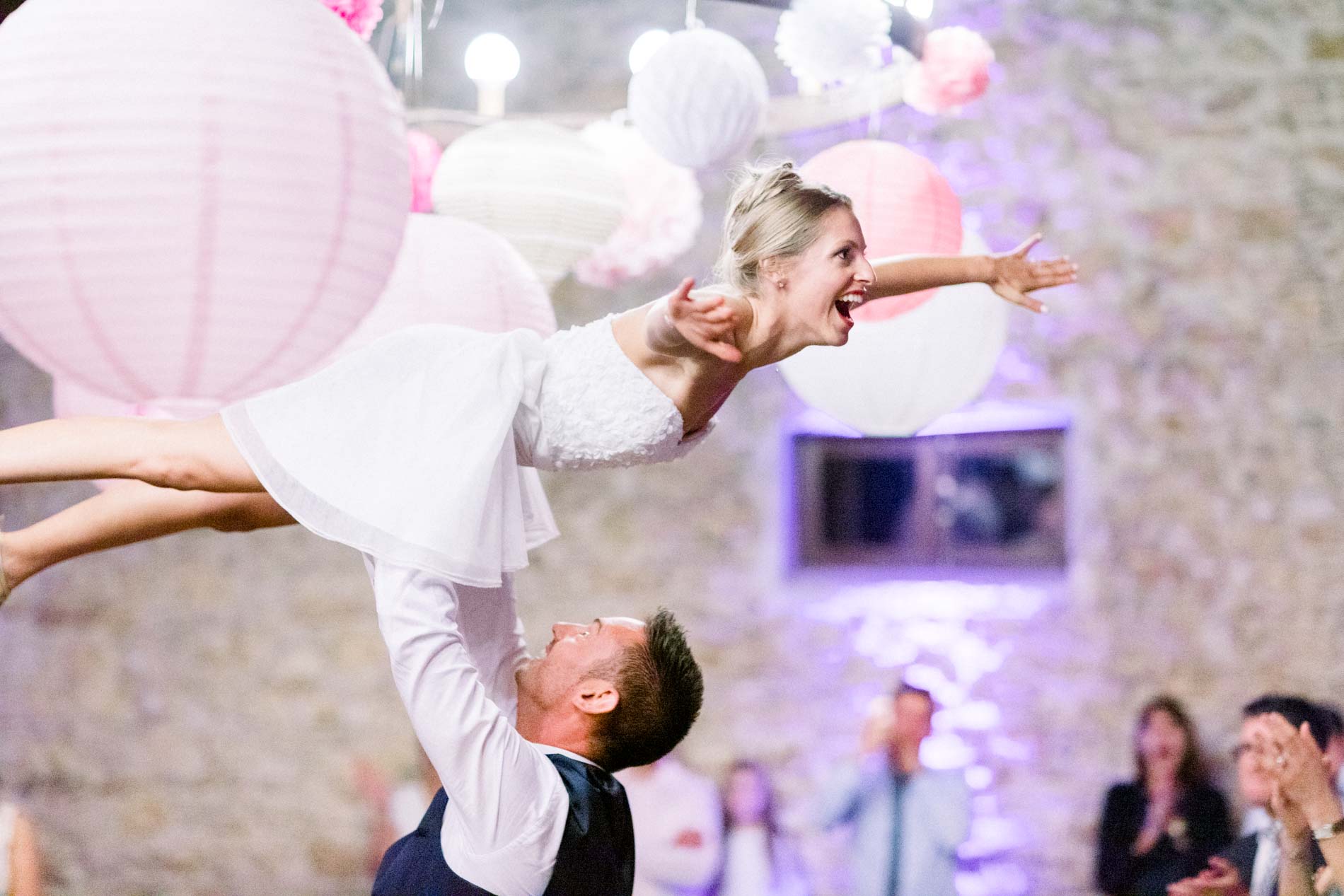 Groom lifting the bride Dirty Dancing style beneath pink lanterns