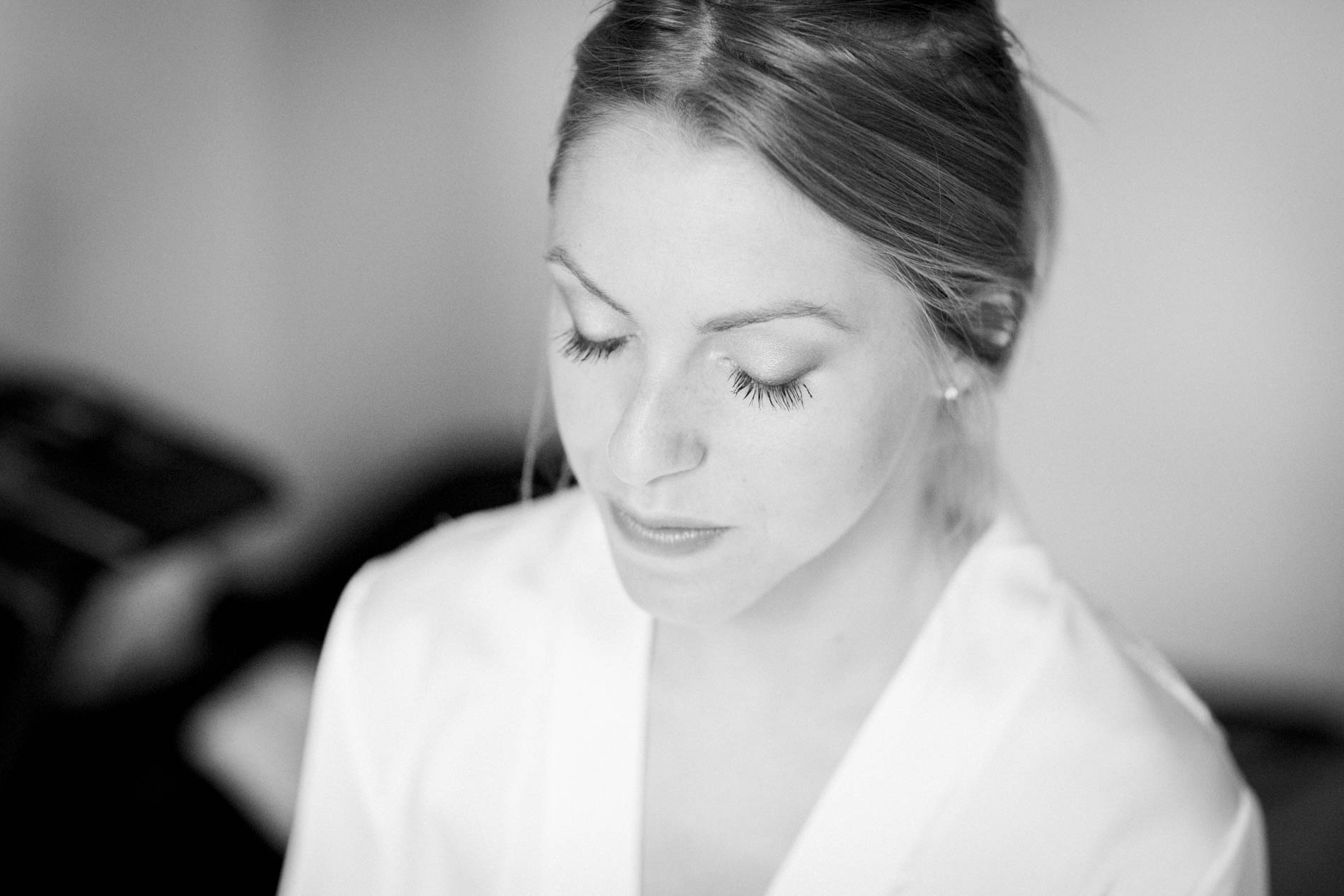 Black and white portrait of the bride in her robe, eyes lowered, while getting ready