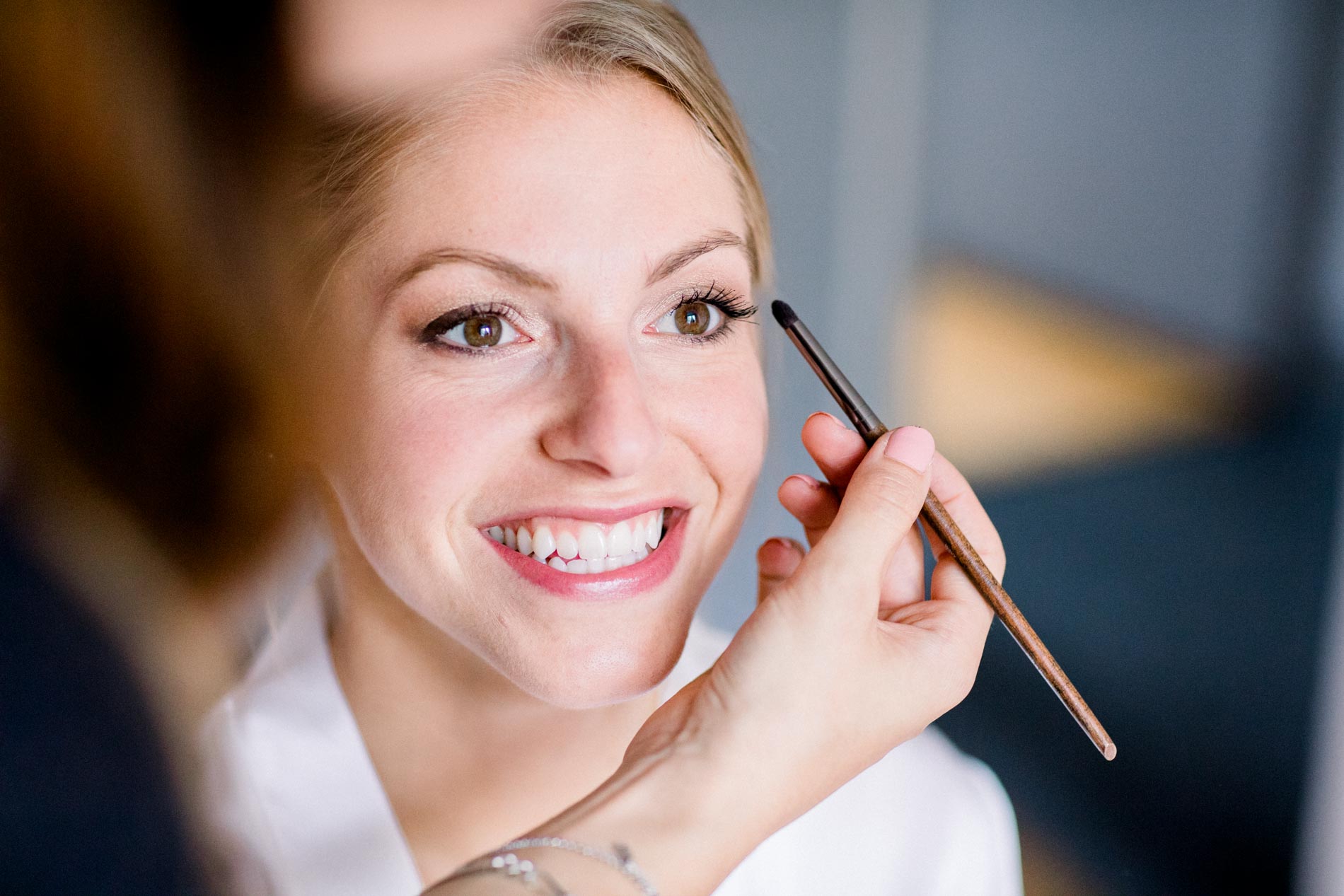 Smiling bride having her make-up applied with a brush close to her face