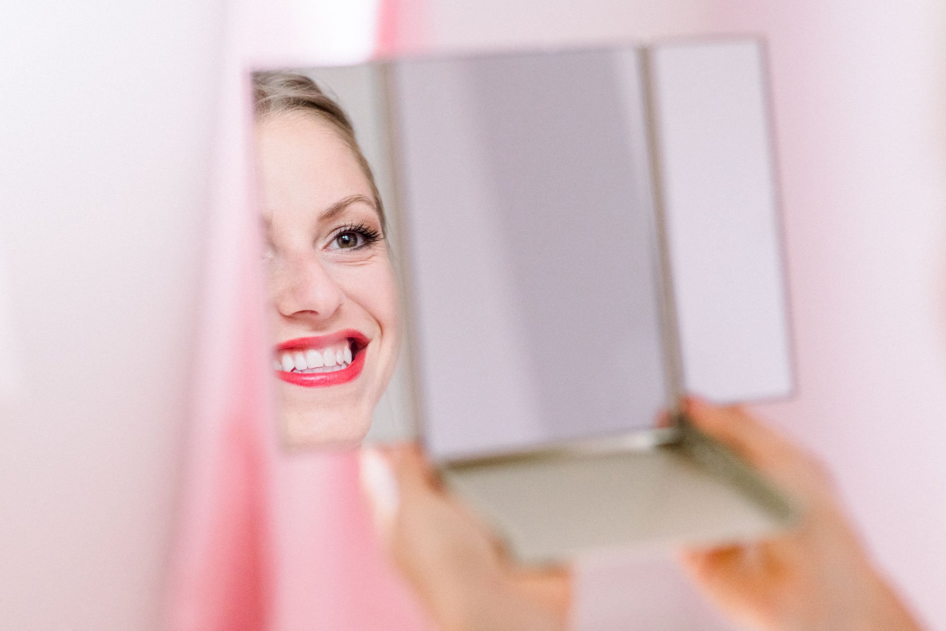 Bride with red lipstick checking her reflection in a pocket mirror