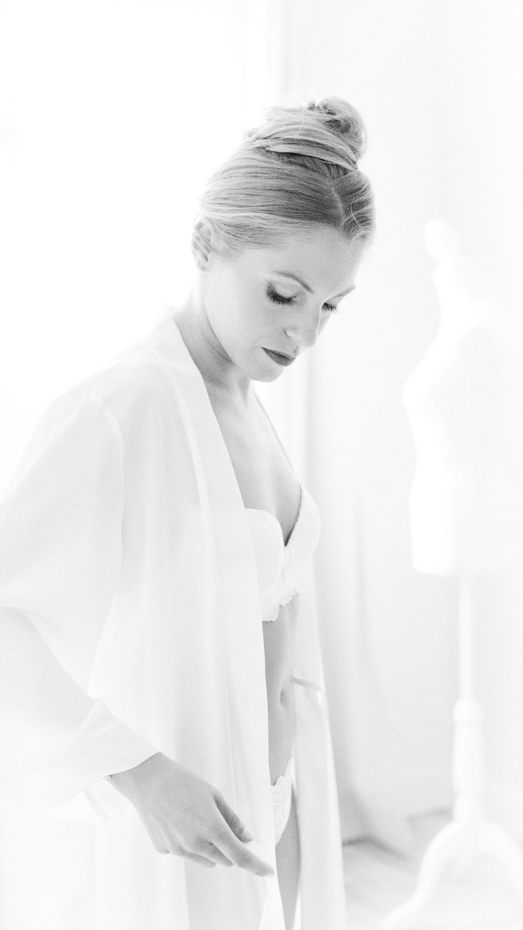 Bride in her robe looking down in soft light, in black and white