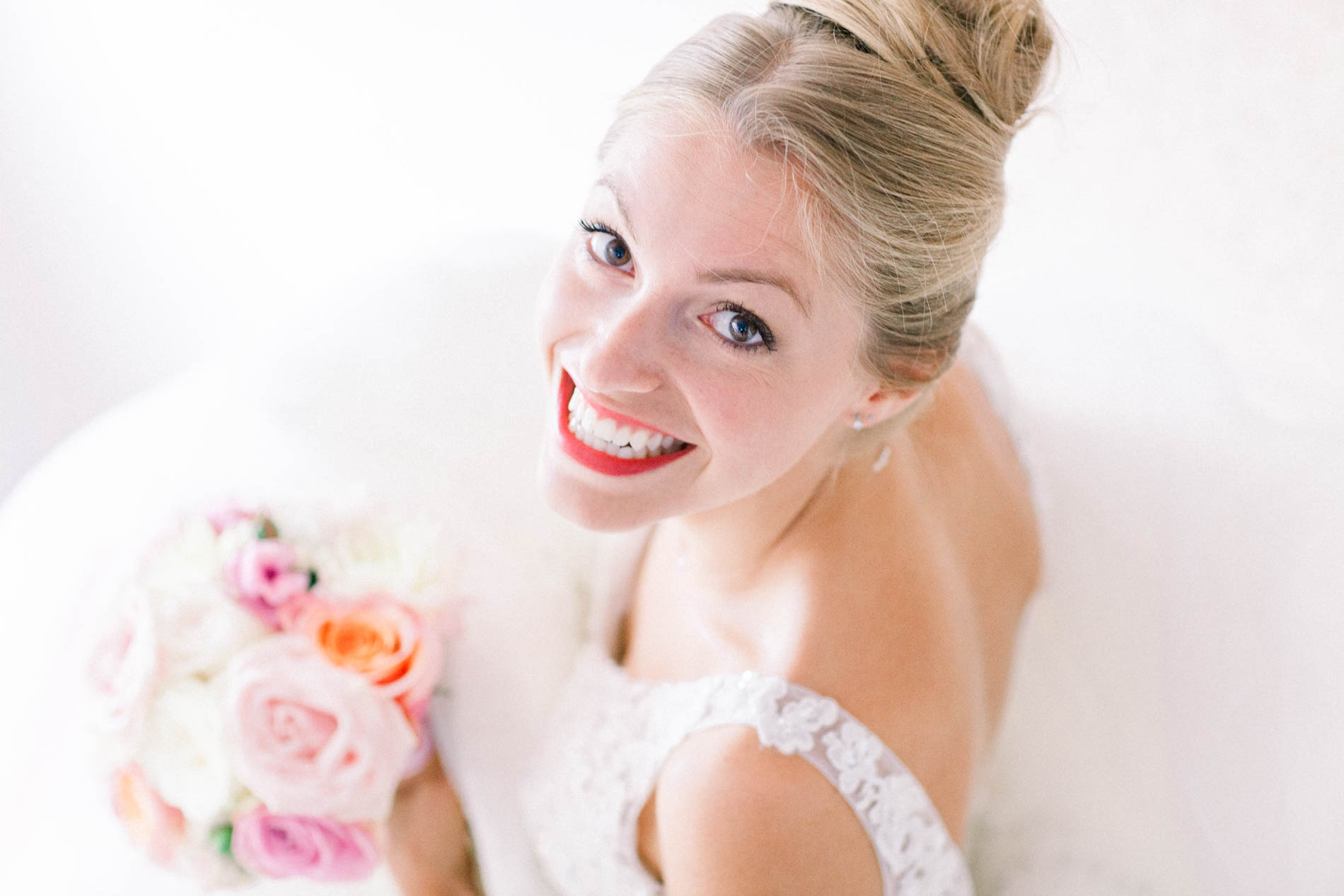 Bride in her gown smiling up at the camera, holding a pastel rose bouquet