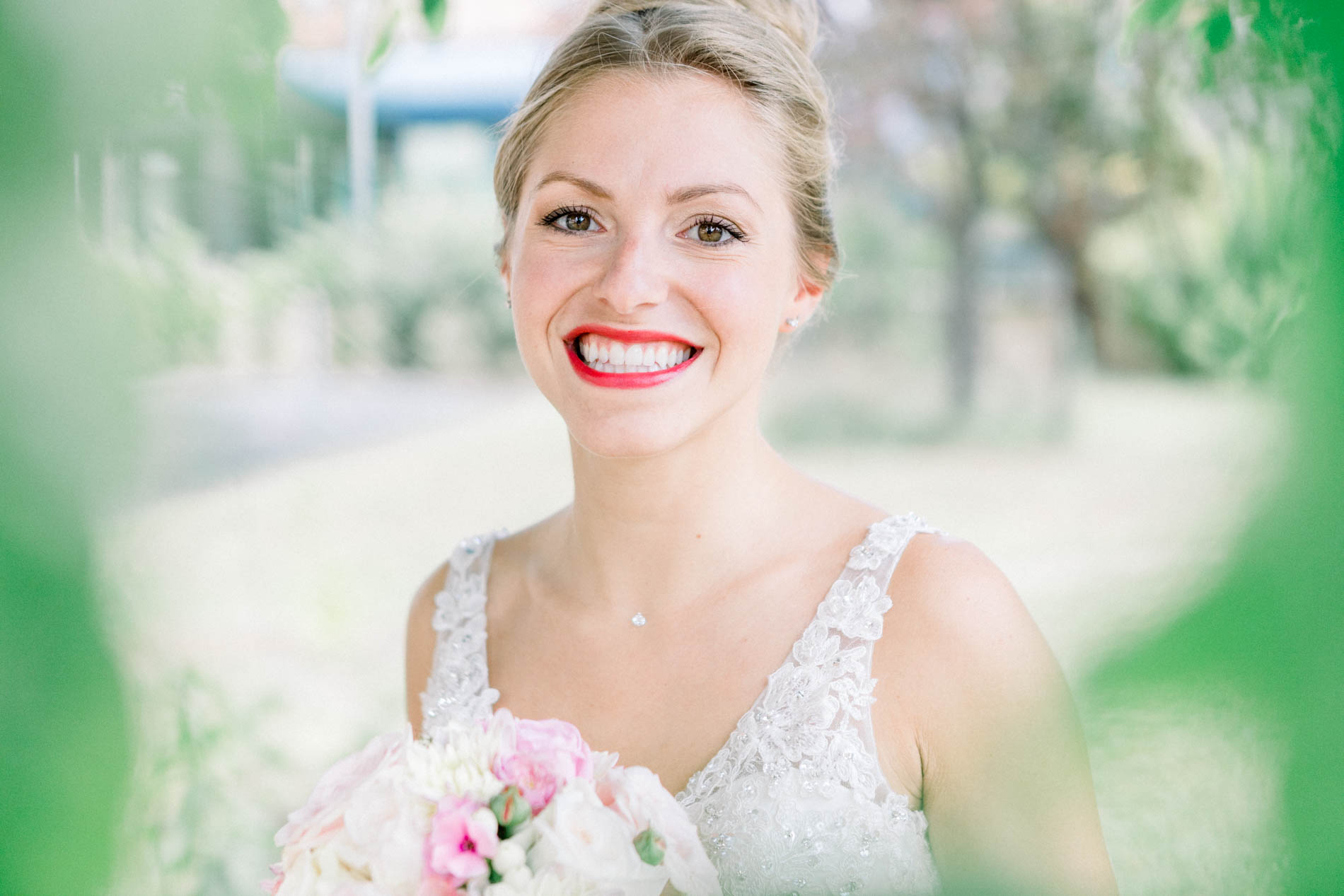 Smiling bride framed by green foliage, holding her bouquet