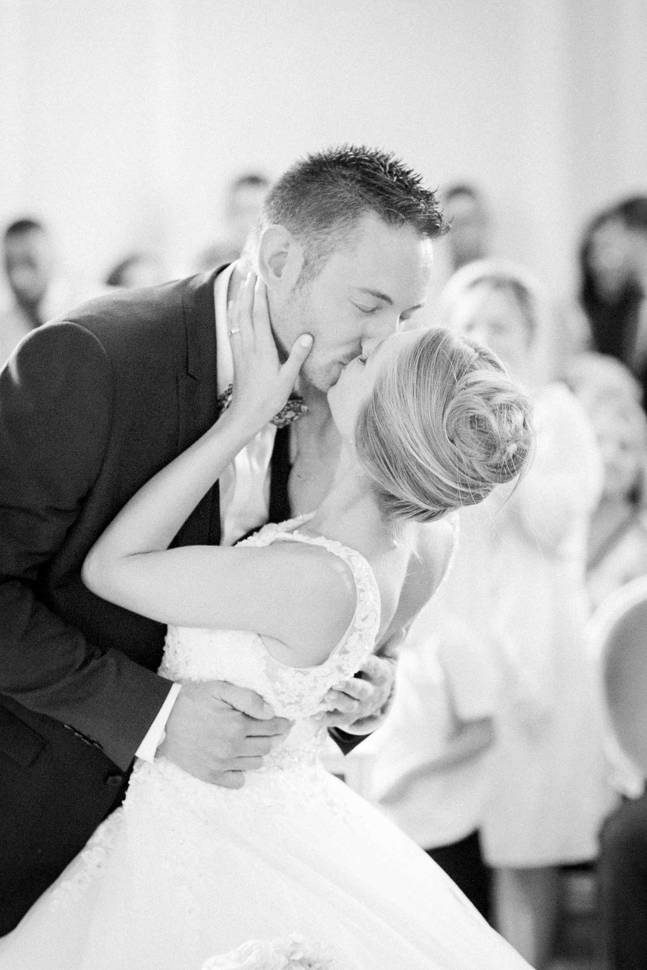 Groom dipping and kissing the bride in front of their guests, in black and white