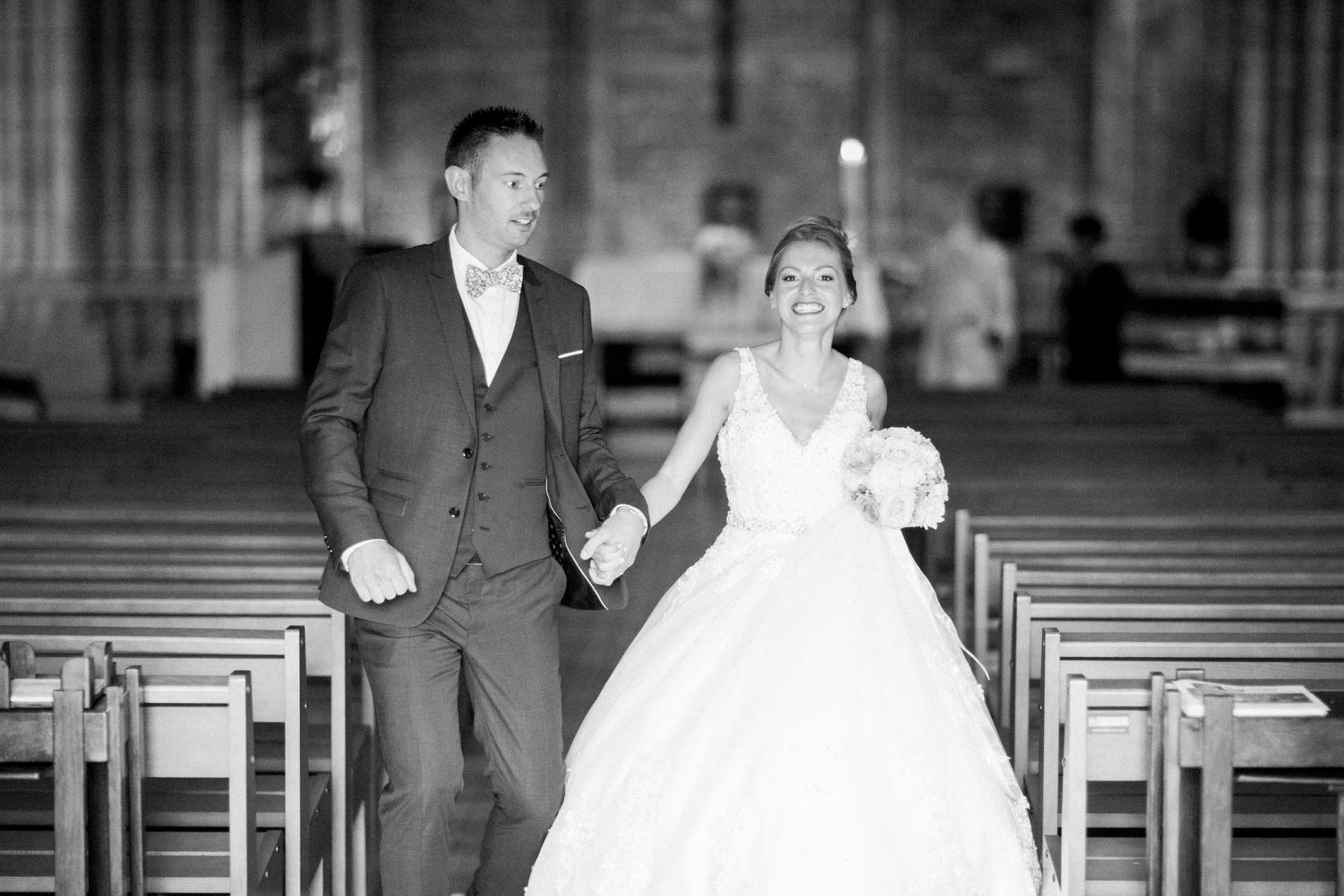 The newlyweds walking back down the church aisle hand in hand, in black and white