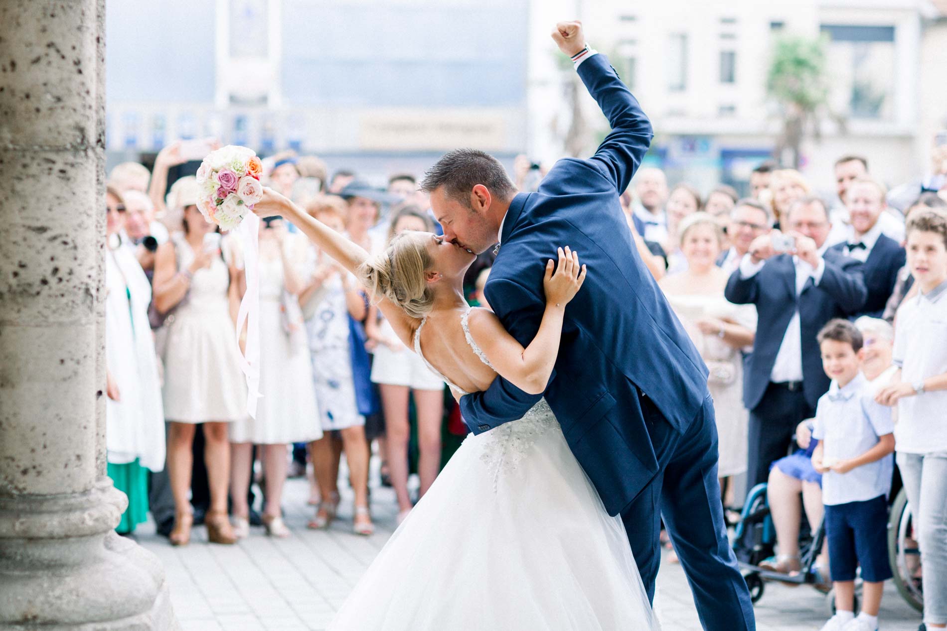 Groom raising his fist as he kisses the bride outside the church with guests