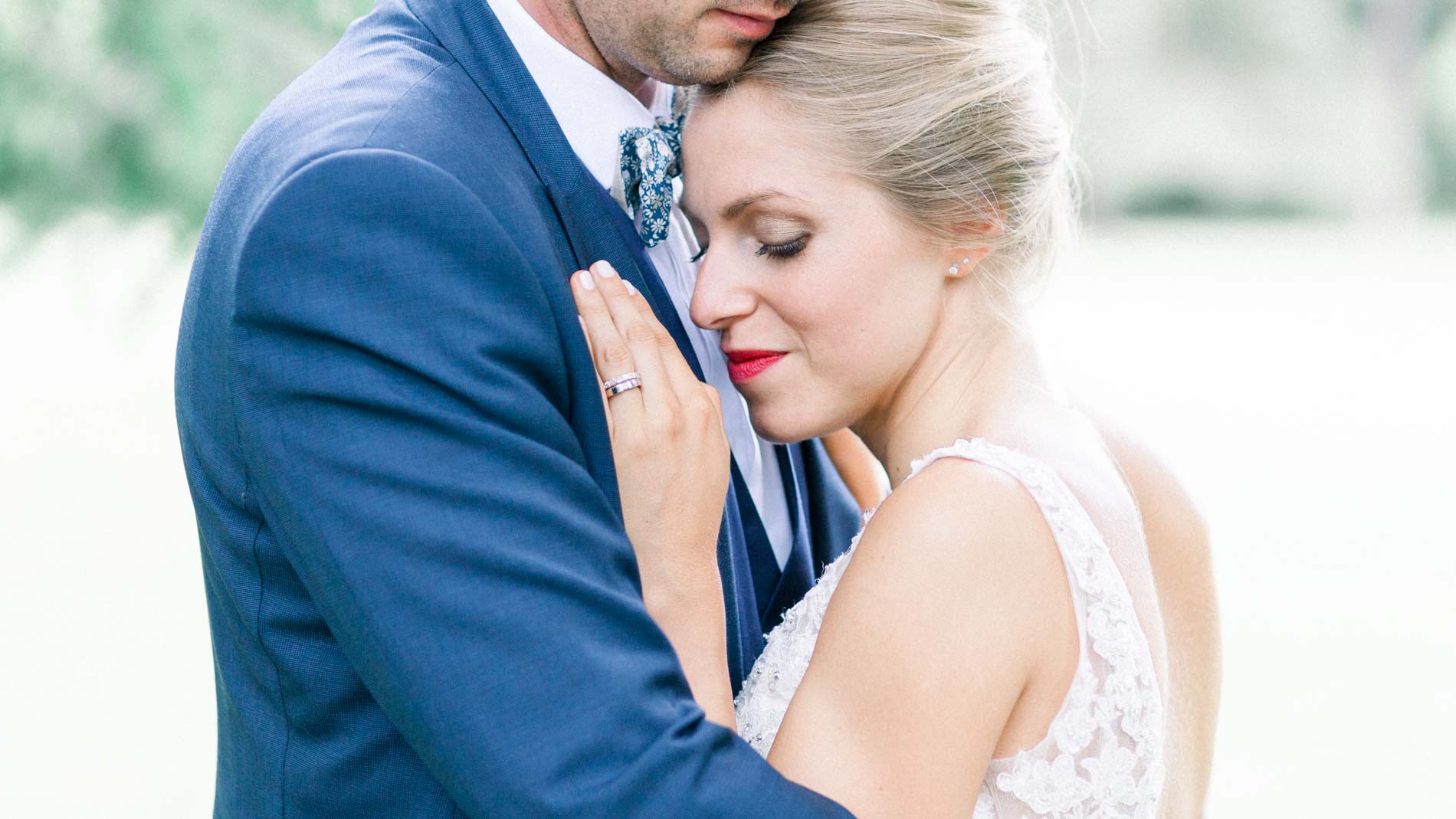 Tender close-up of the bride, eyes closed, against the groom's blue suit