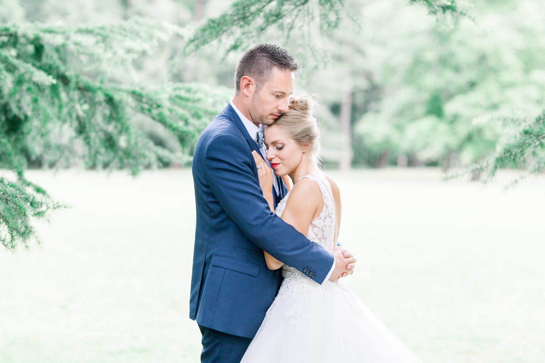 Bride and groom embracing beneath a cedar, the bride's eyes closed
