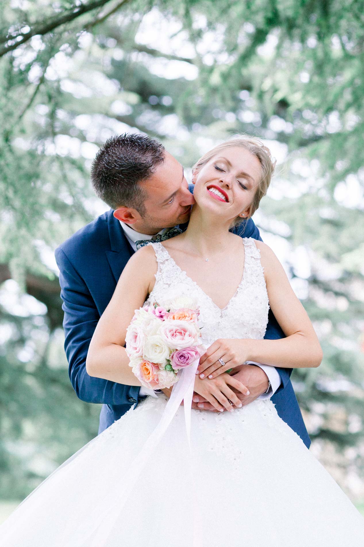 Groom kissing the bride's cheek as she holds her rose bouquet