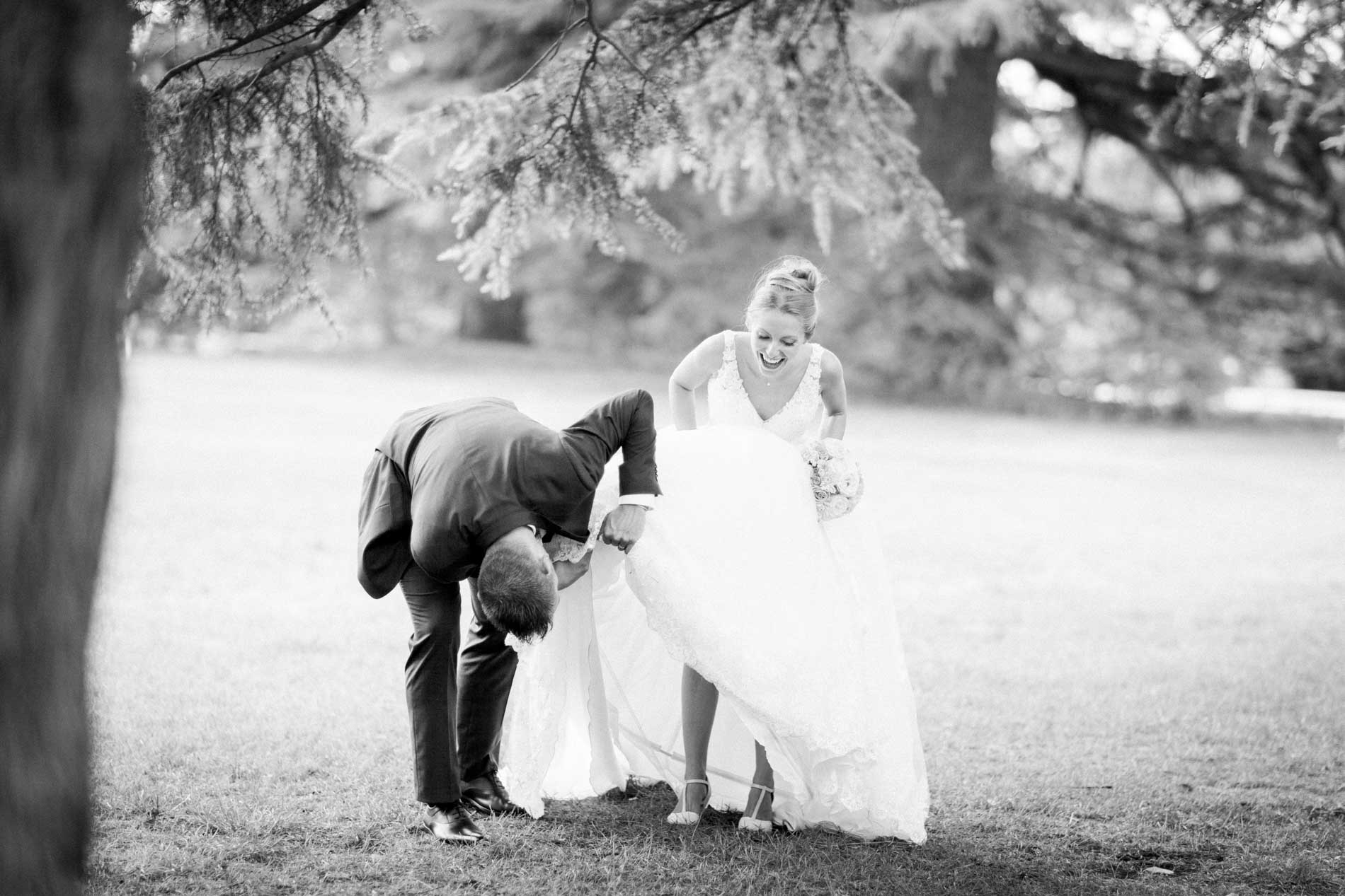 Groom bending towards the bride's dress in the park, in black and white