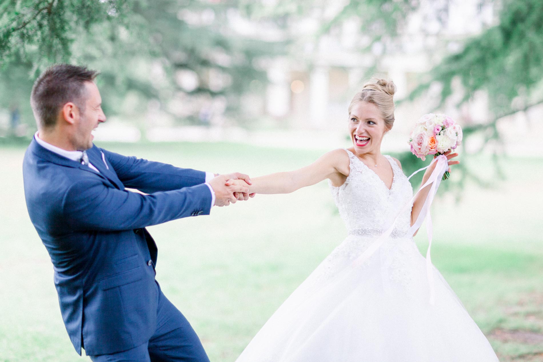 Bride and groom playfully pulling each other by the hand on the château lawn