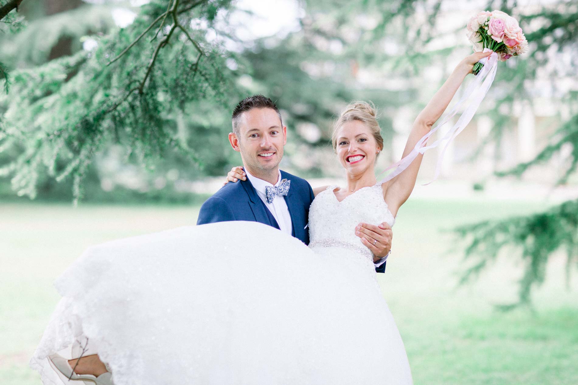 Groom carrying the bride, bouquet raised, on the lawn at Château de Cujac