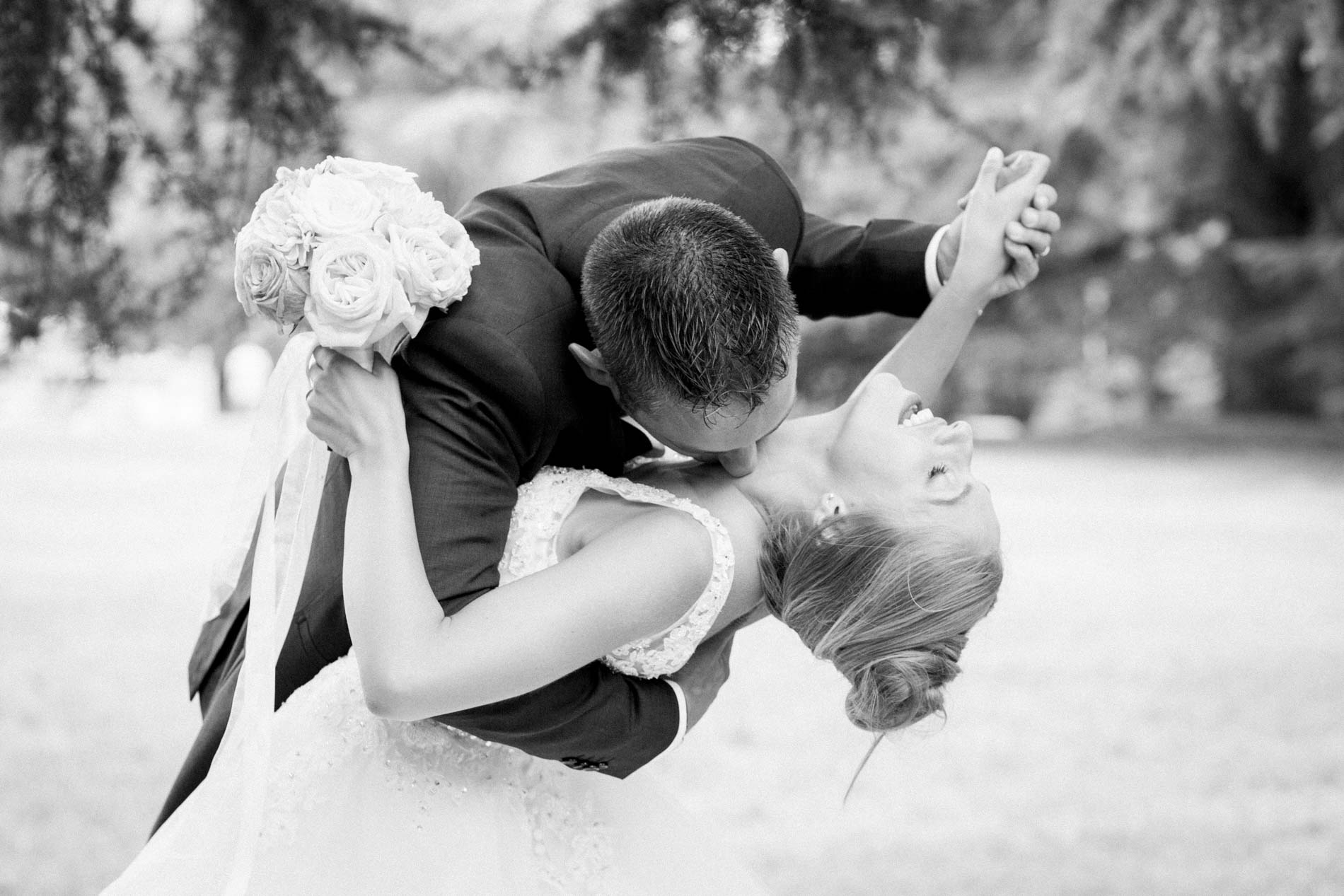 Groom dipping the bride for a kiss, her bouquet raised, in black and white