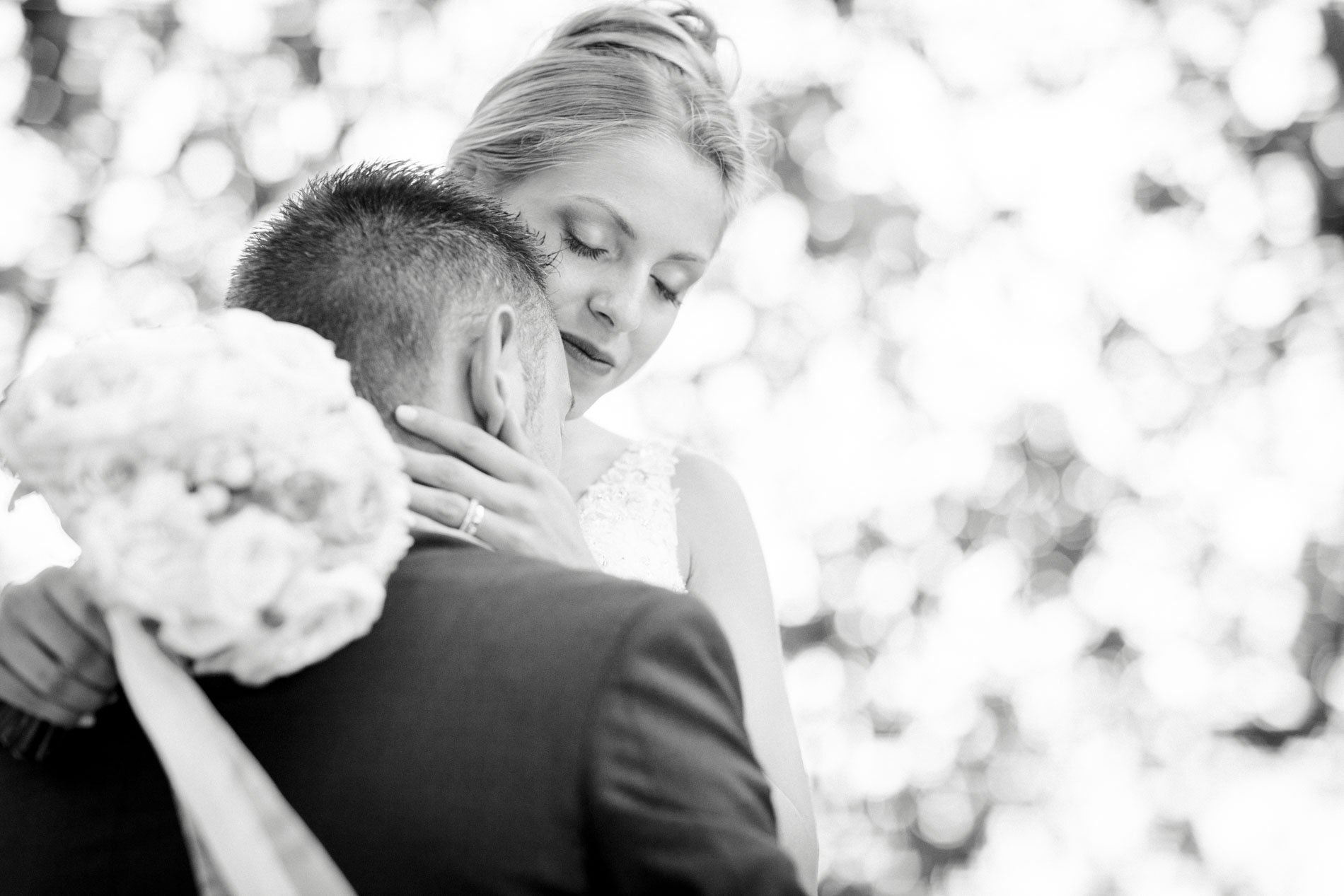 Groom resting his head against the bride holding her bouquet, in black and white