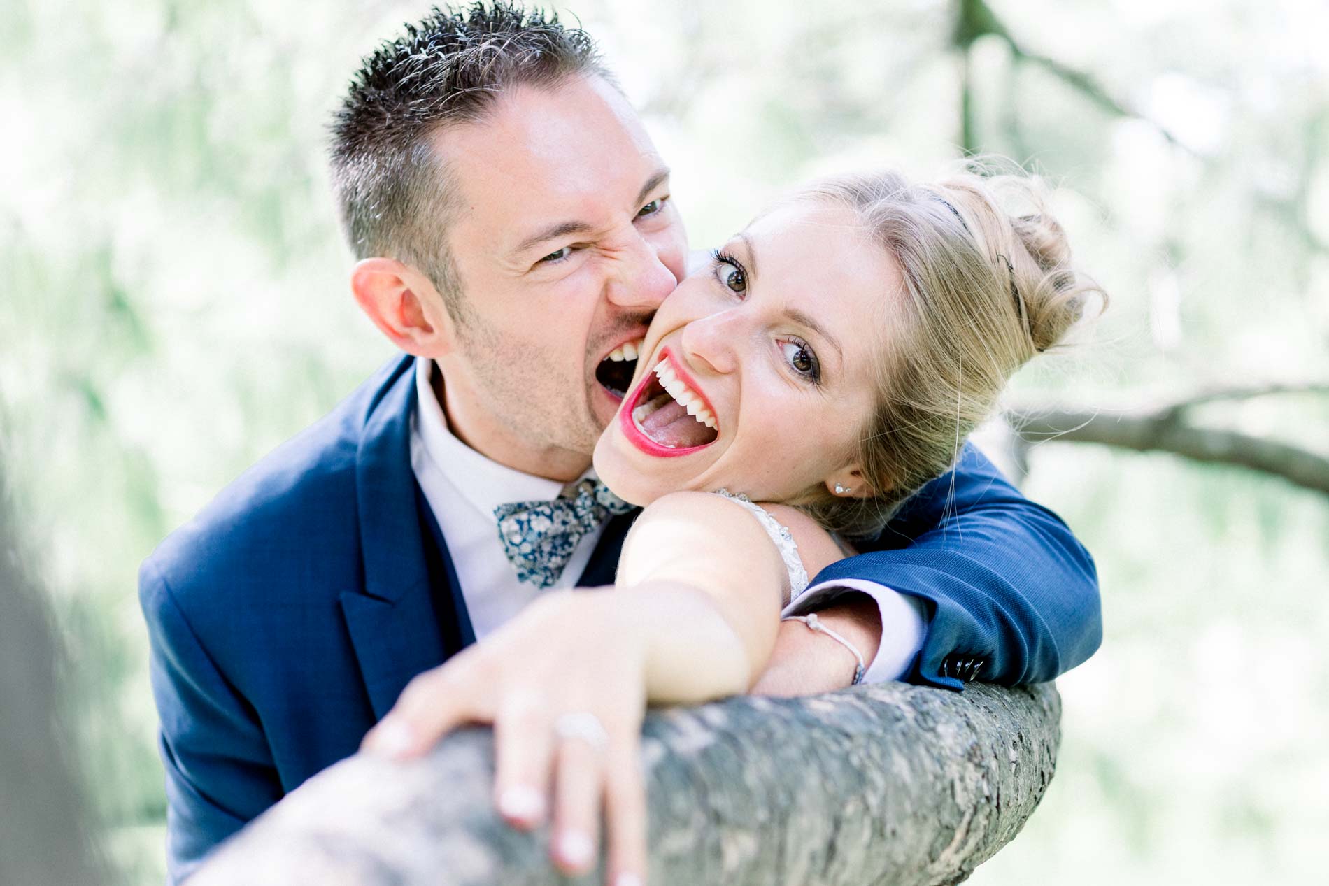 Bride and groom bursting into laughter while leaning on a tree branch