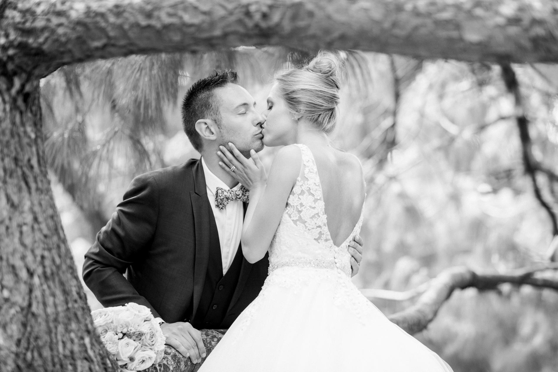 Bride and groom kissing framed by tree branches, in black and white