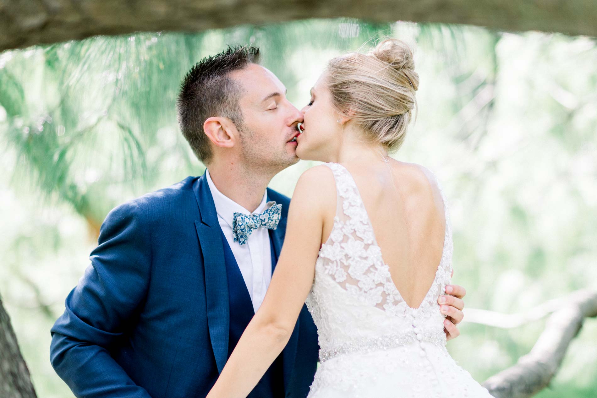 Bride and groom kissing by a tree, the bride in a lace-back gown