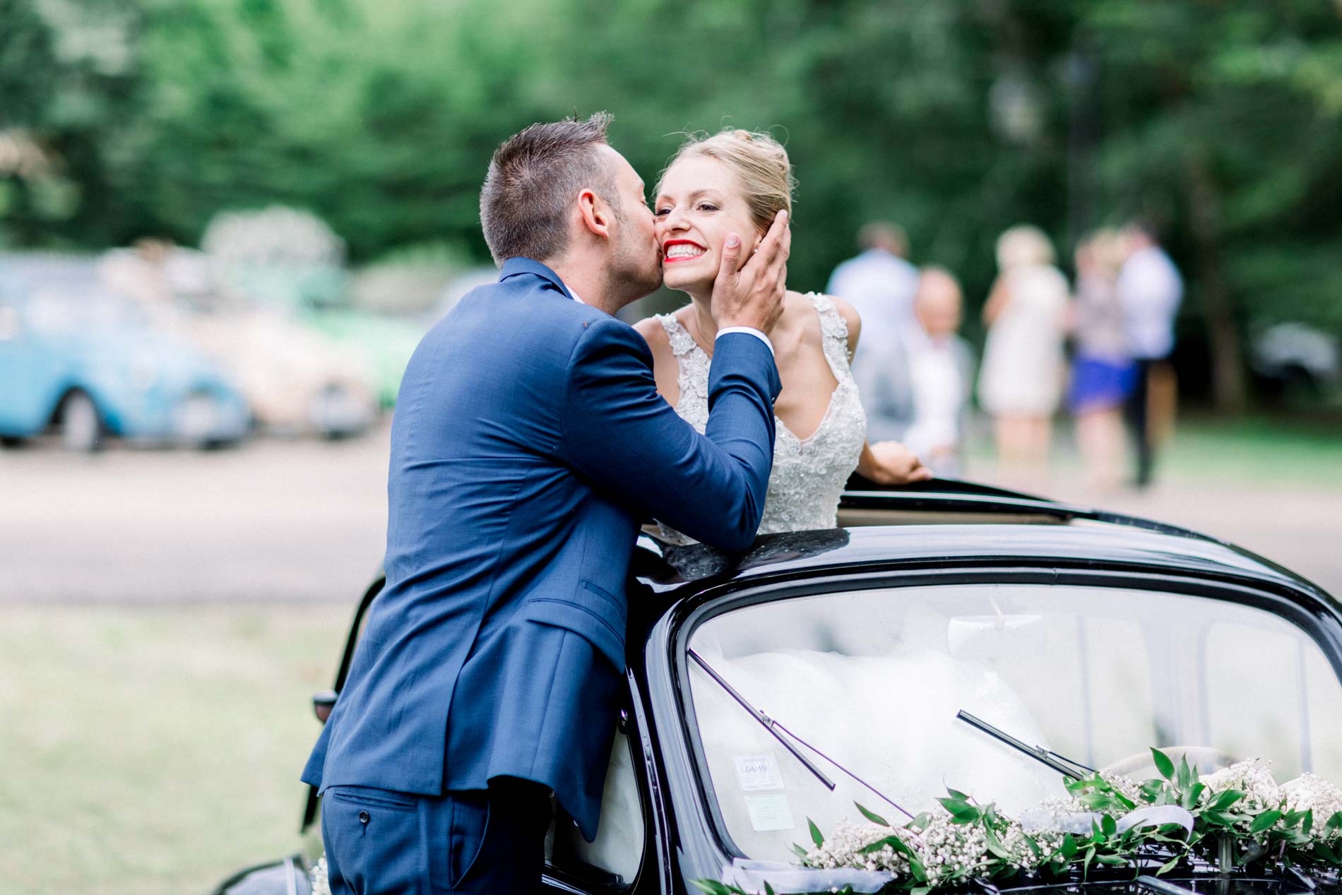 Groom kissing the bride as she sits on the vintage car door