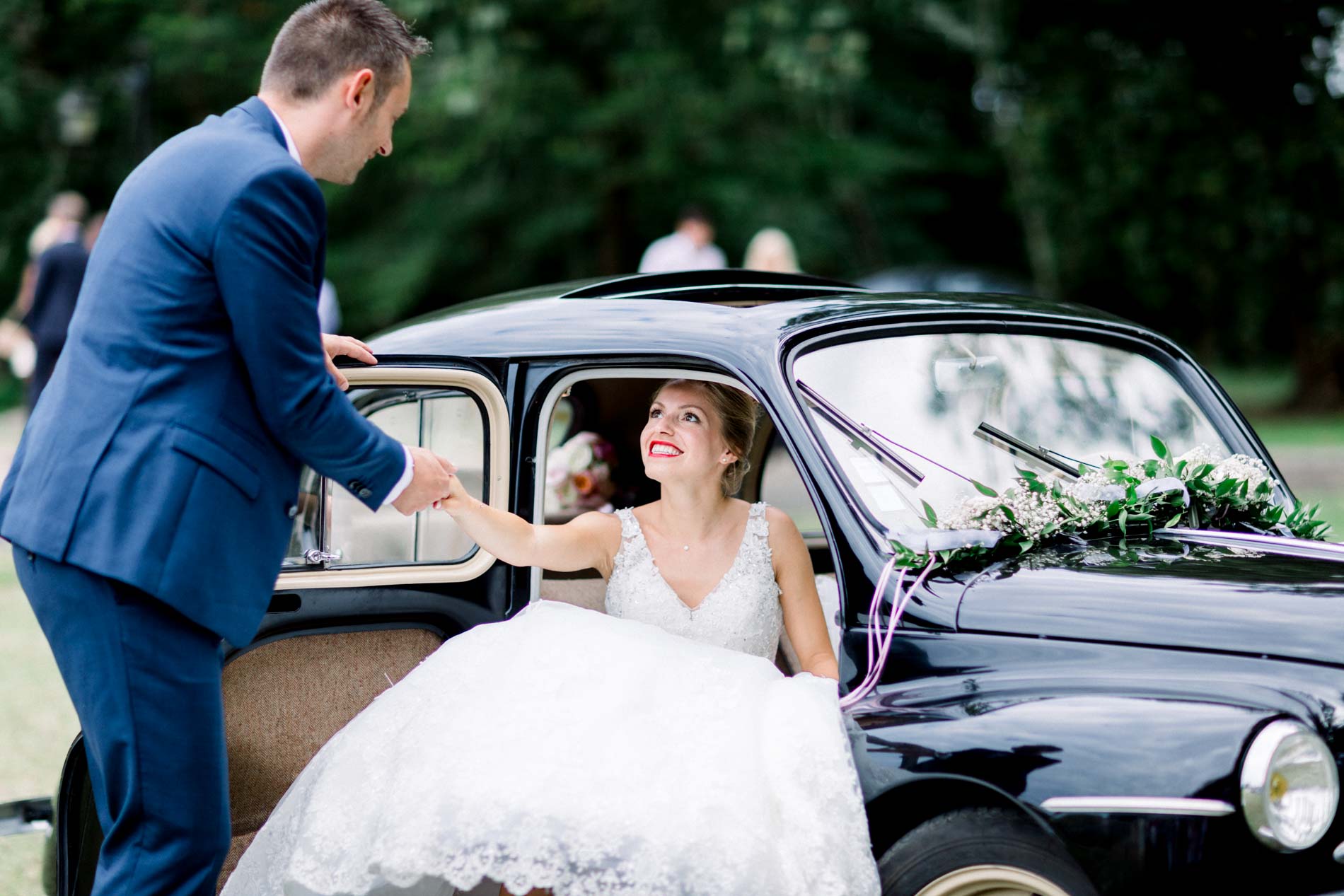 Groom helping the bride out of the black vintage car decorated with flowers