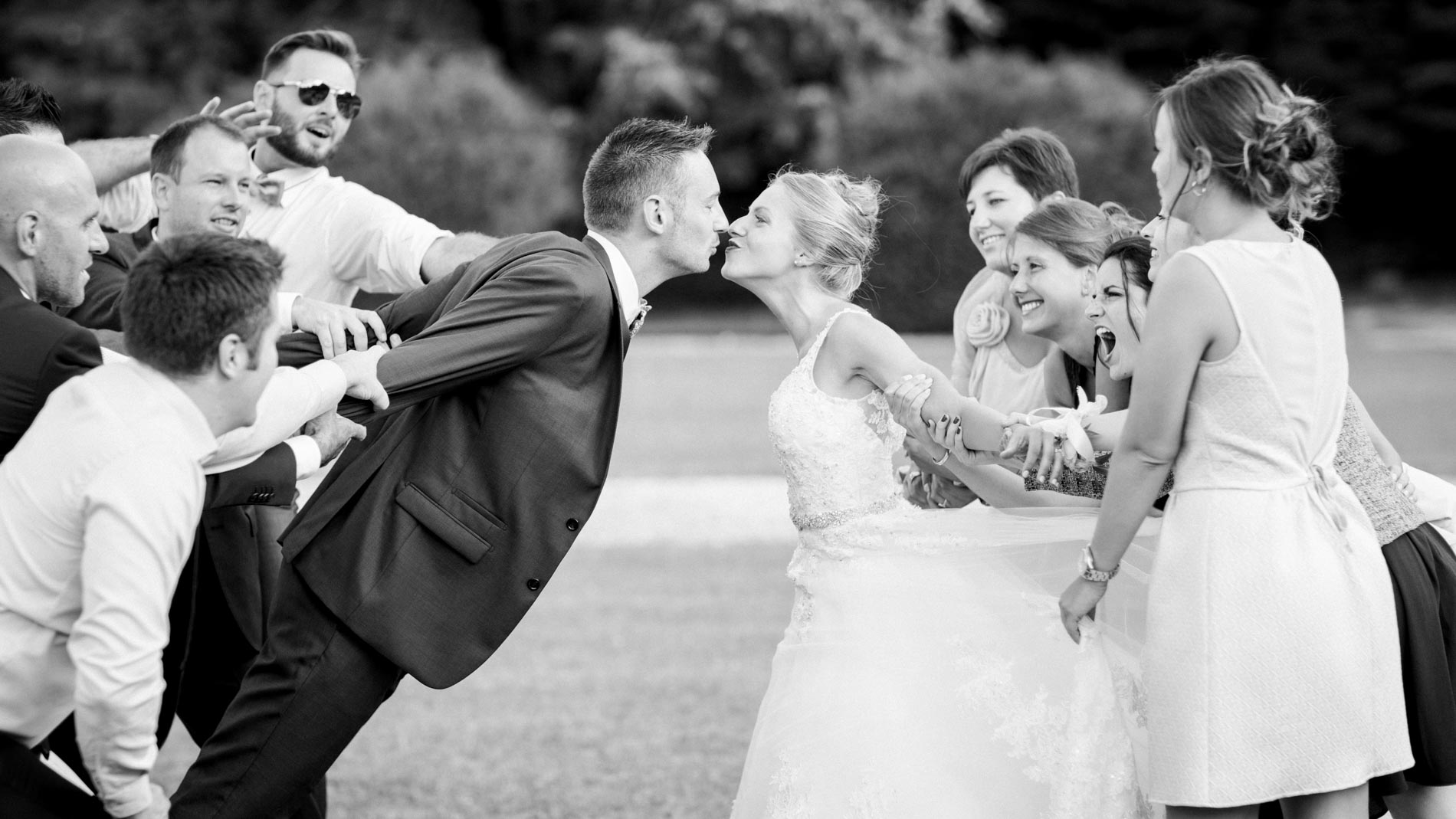 Bride and groom kissing as their guests mimic them, in black and white
