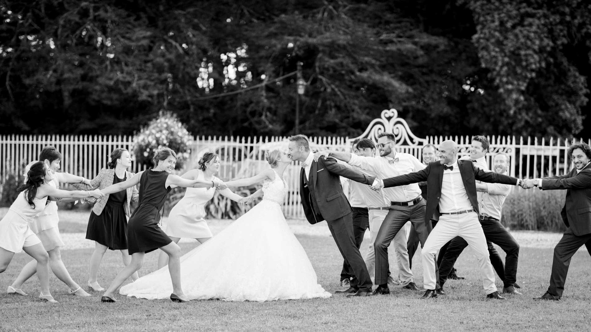 Guests forming a playful leg-raised guard of honour on the lawn, in black and white