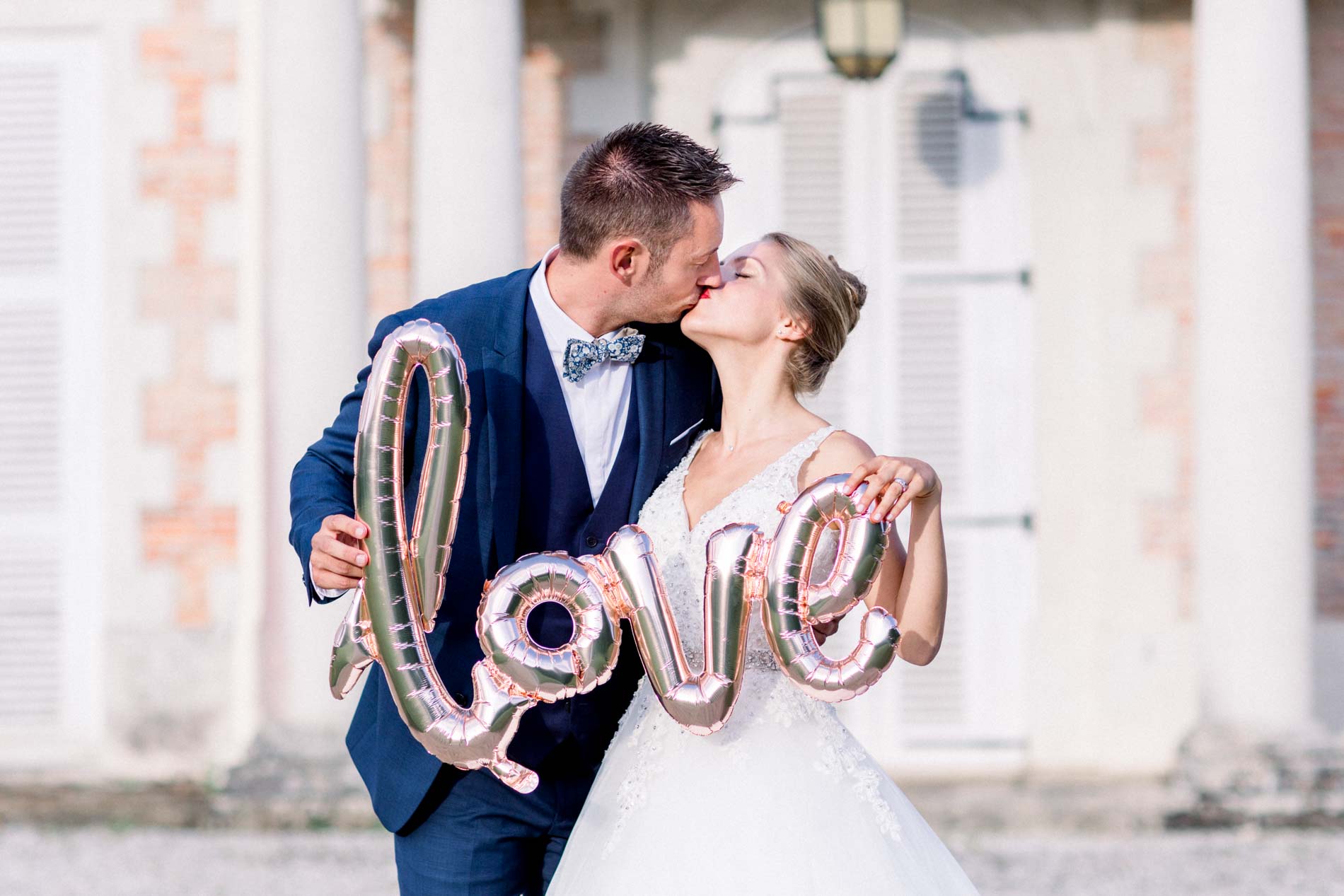Bride and groom kissing behind a gold love balloon in front of the château