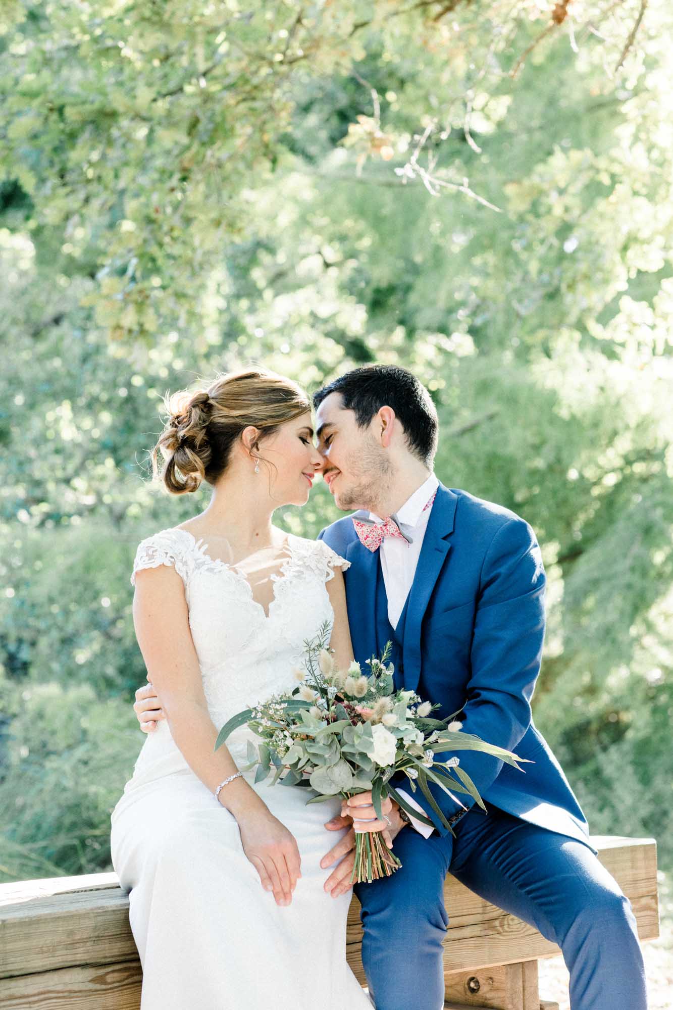Couple sitting on a wooden bench nose to nose, with a country-style bouquet
